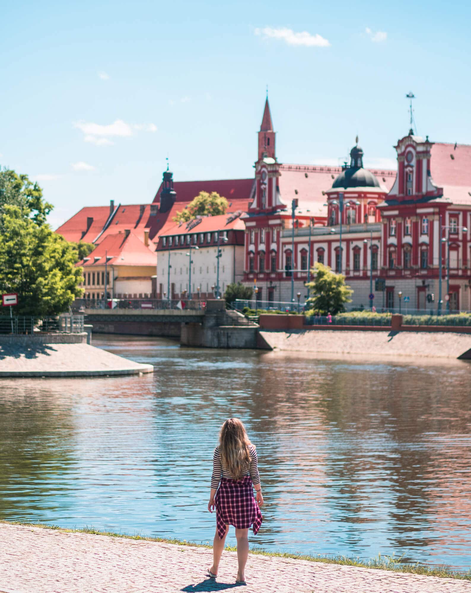 Wroclaw Poland. Girl with long hair, wearing a striped dress and purple shirt, walking along the river in Wroclaw with red old buildings in the background.