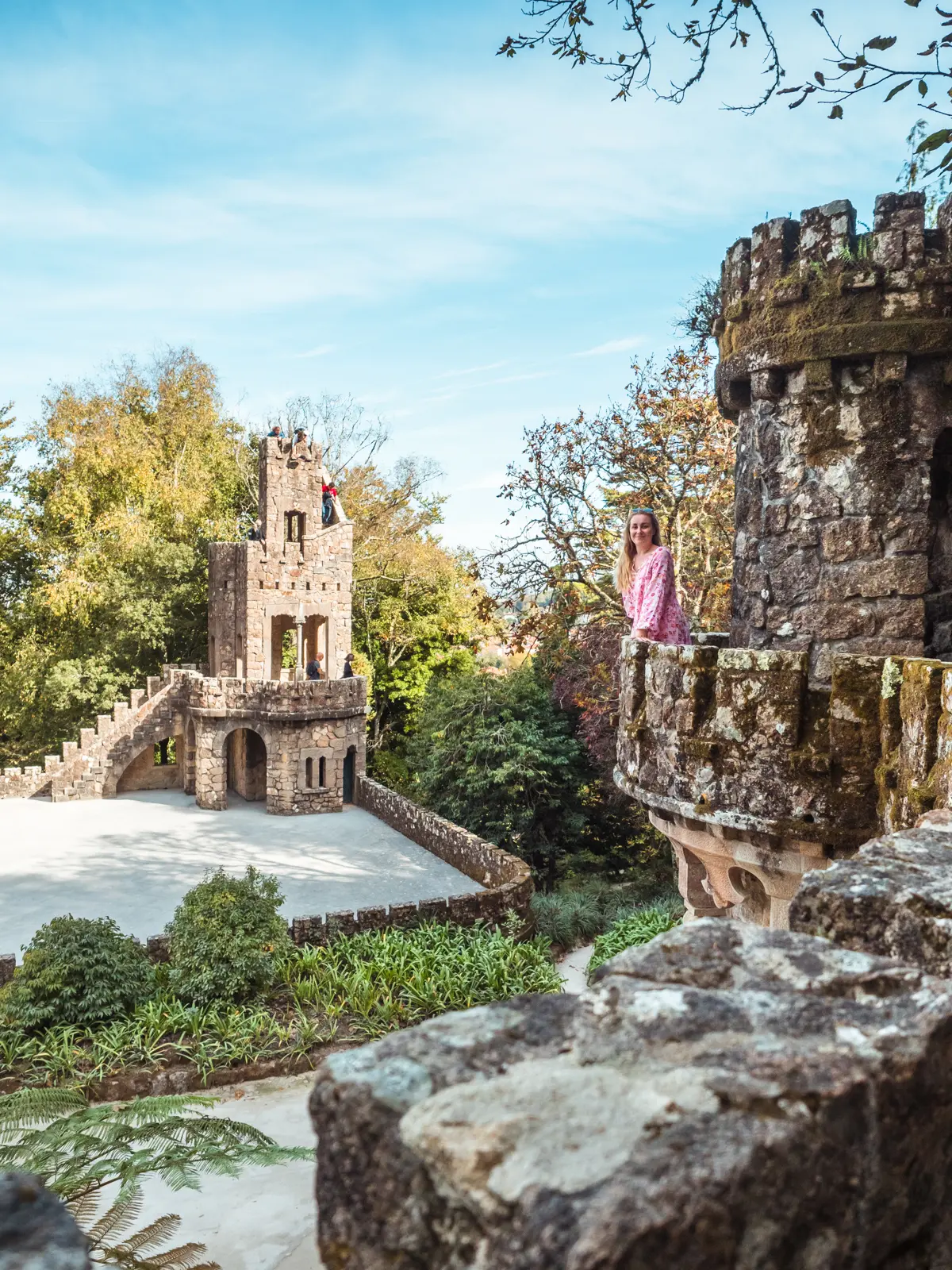 Girl in pink dress looking towards the camera from a stone tower at Quinta da Regaleira, the most beautiful palace in Sintra.