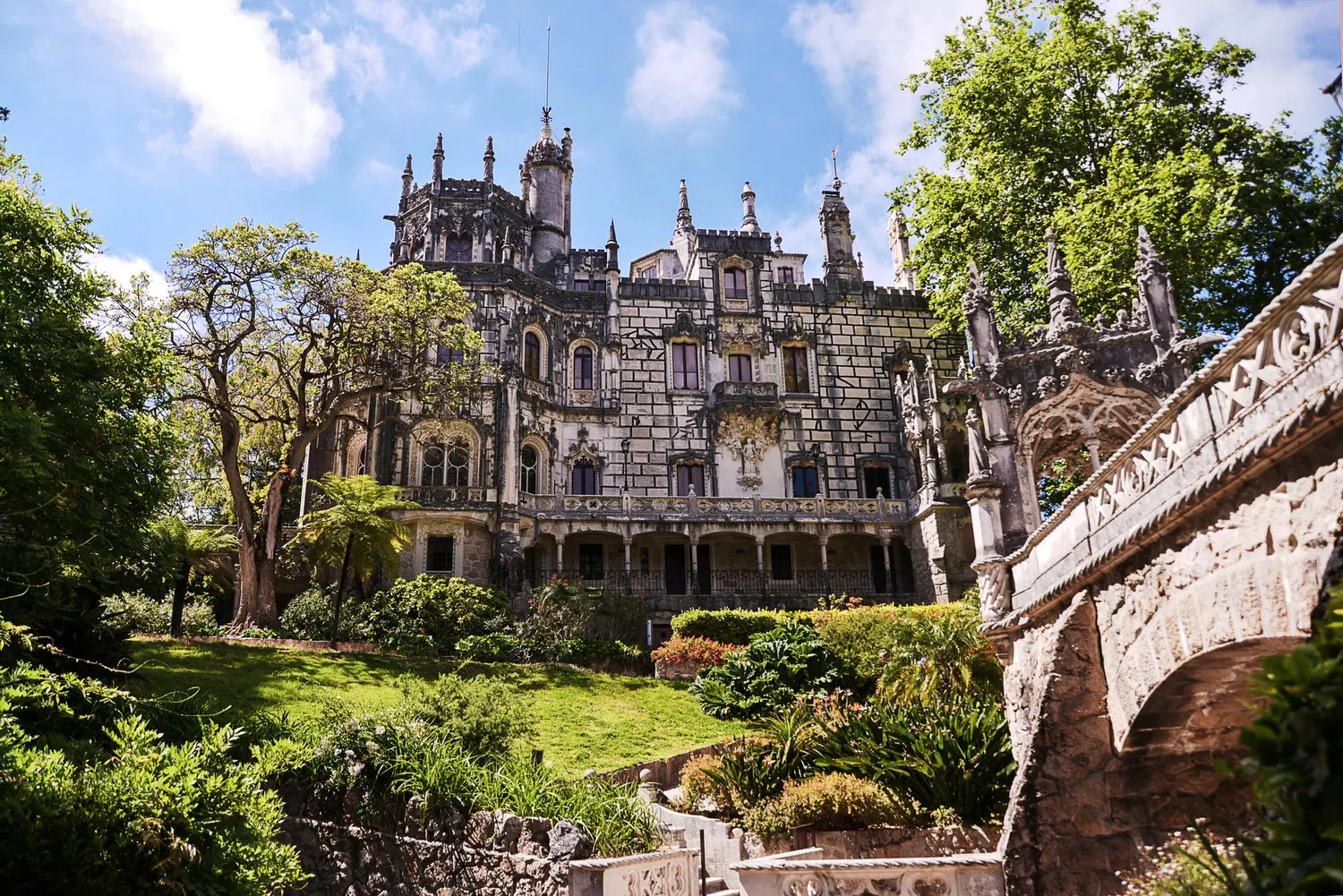 Ornate 19th century Quinta da Regaleira stone palace with spires in Sintra Portugal, surrounded by green gardens.