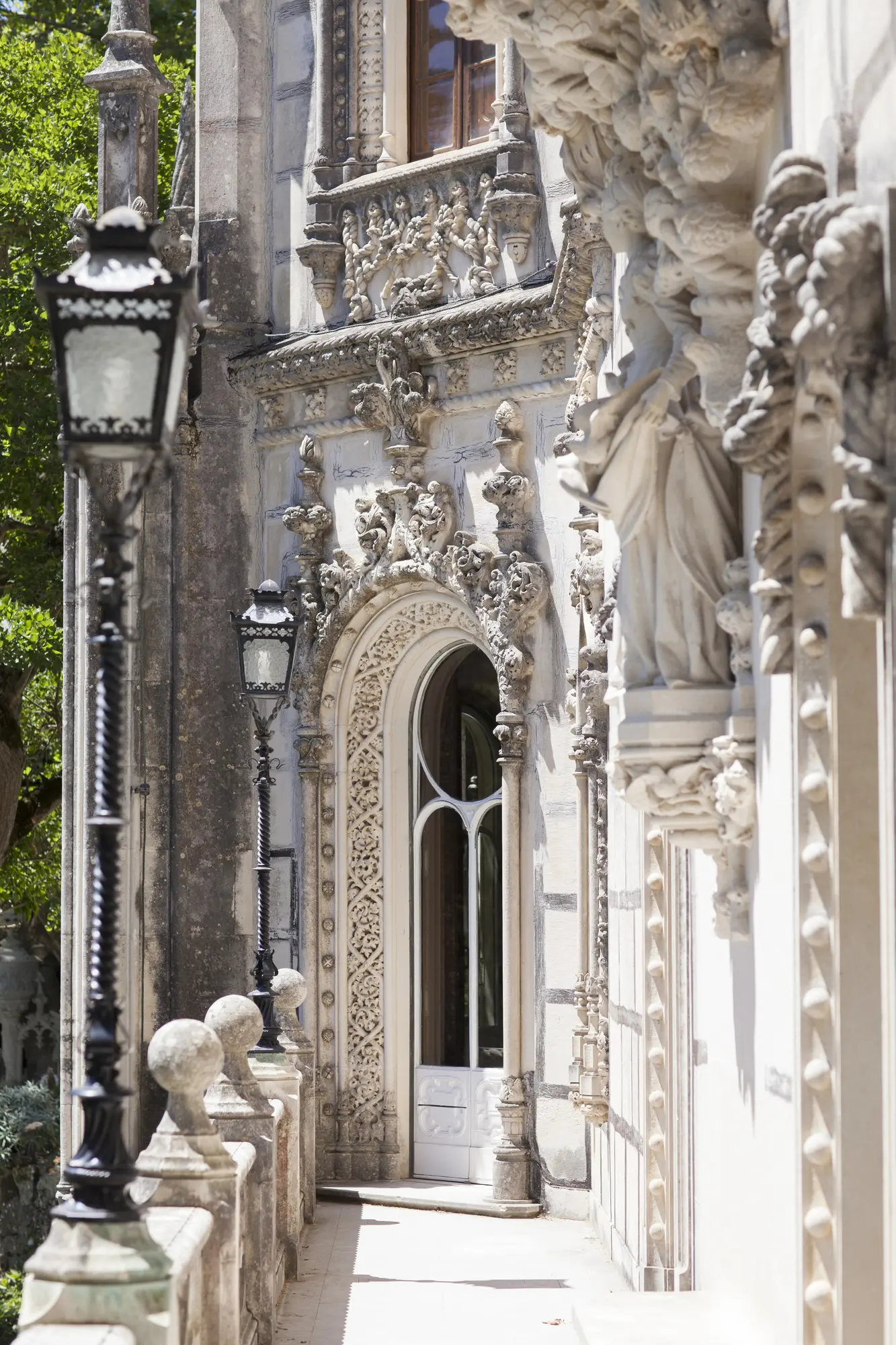 Close up of ornate white and grey stone balcony and rod iron street lamp at Quinta da Regaleira palace in Sintra Portugal.