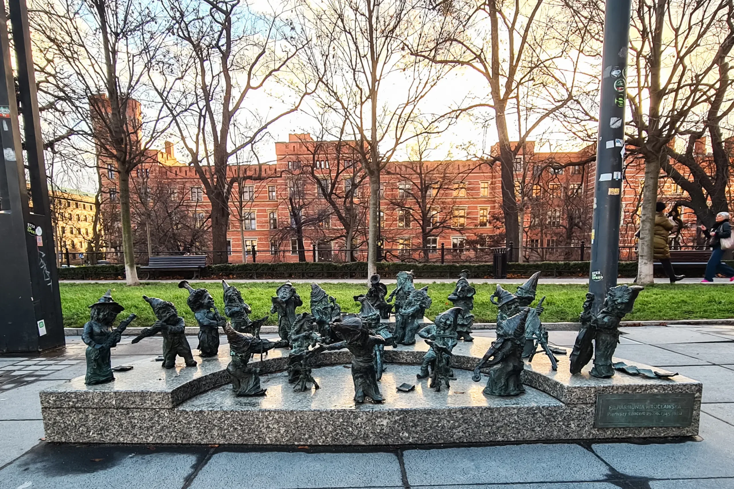 Collection of 18 metal dwarfs on a stone slab with a large brick building in the background in Wroclaw.