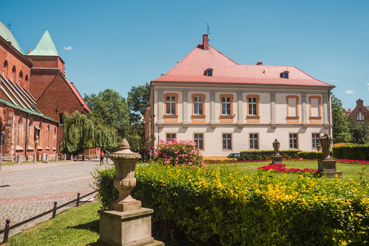 Part of brick church and an old white, light green and orange building surrounded by a green lawn in Wroclaw Poland.
