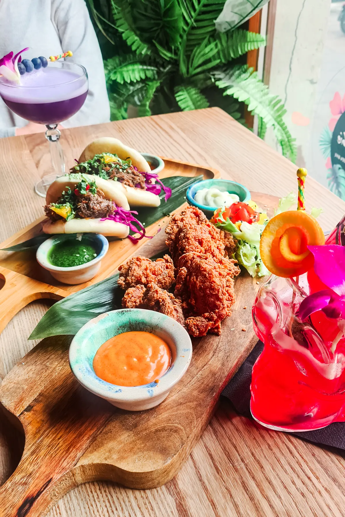 Fried chicken with chipotle sauce and pulled beef bao buns on green palm leaf on wooden trays at Hawajskie Niebo w Gębie, one of the best restaurants in Krakow.