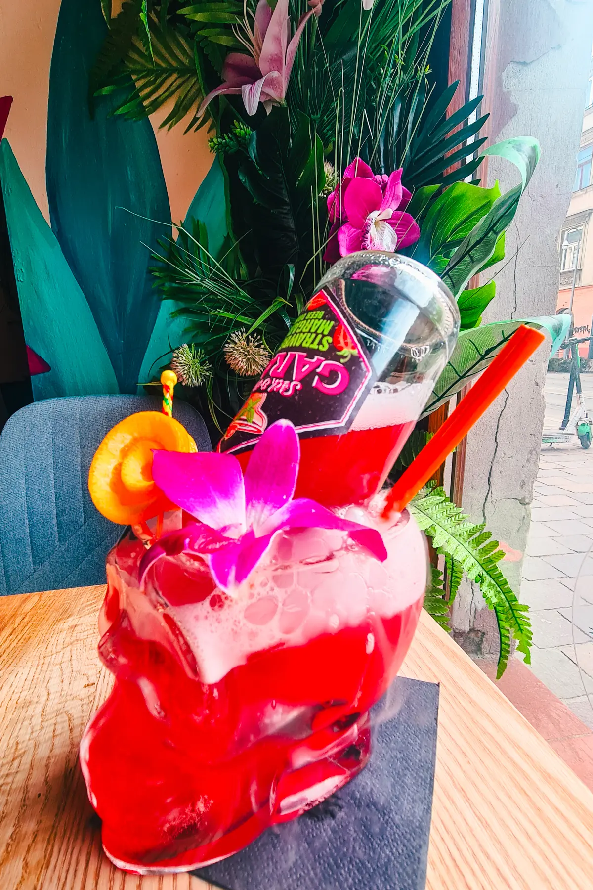 Scull shaped glass with a red drink and a beer bottle sticking out at Hawajskie Niebo w Gębie, one of the best restaurants and cocktail bars in Krakow.