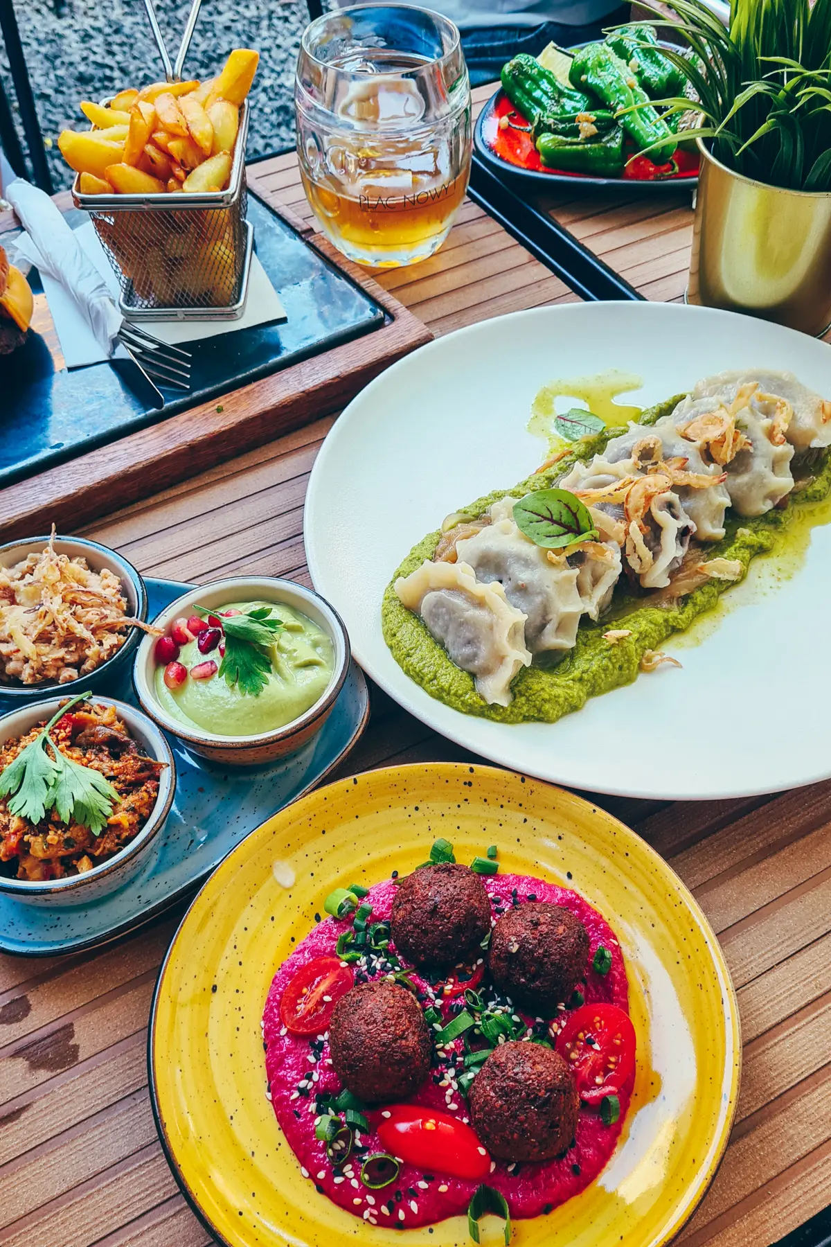 Yellow plate with beet hummus a four falafel, pierogis in green sauce on a white plate and three small dips at at Plac Nowy 1, one of the best restaurants in Krakow.