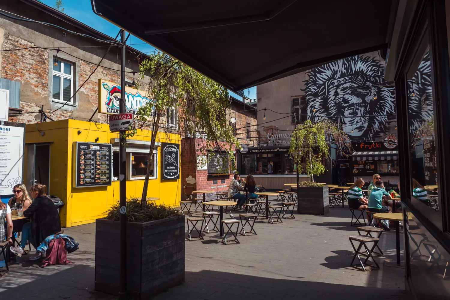 View of a concrete street food market with a yellow food truck on the left and a black and white mural on the right, one of the best places to eat in affordable food in Krakow.