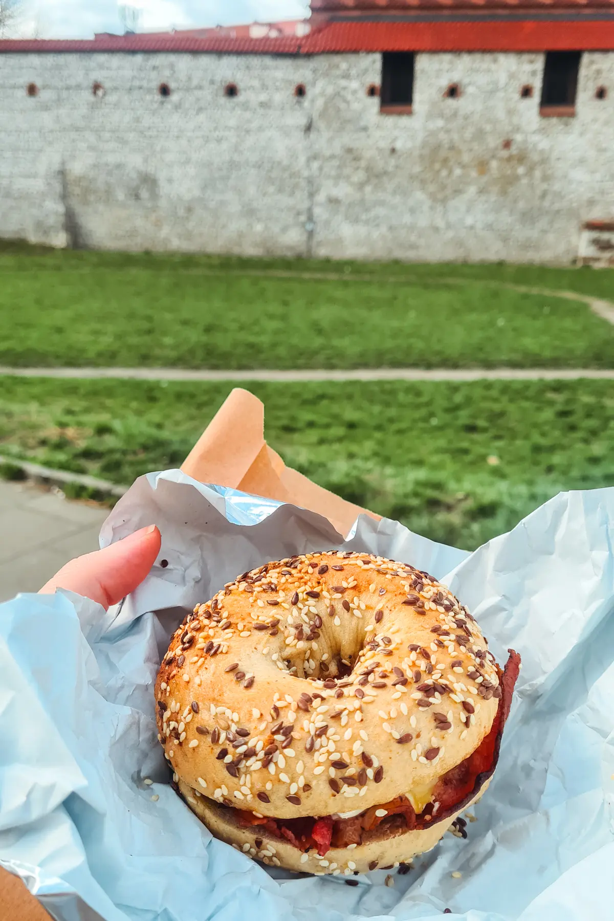 Hand holding a everything bagel on a paper from Bagelmama, one of the best cafés in Krakow.