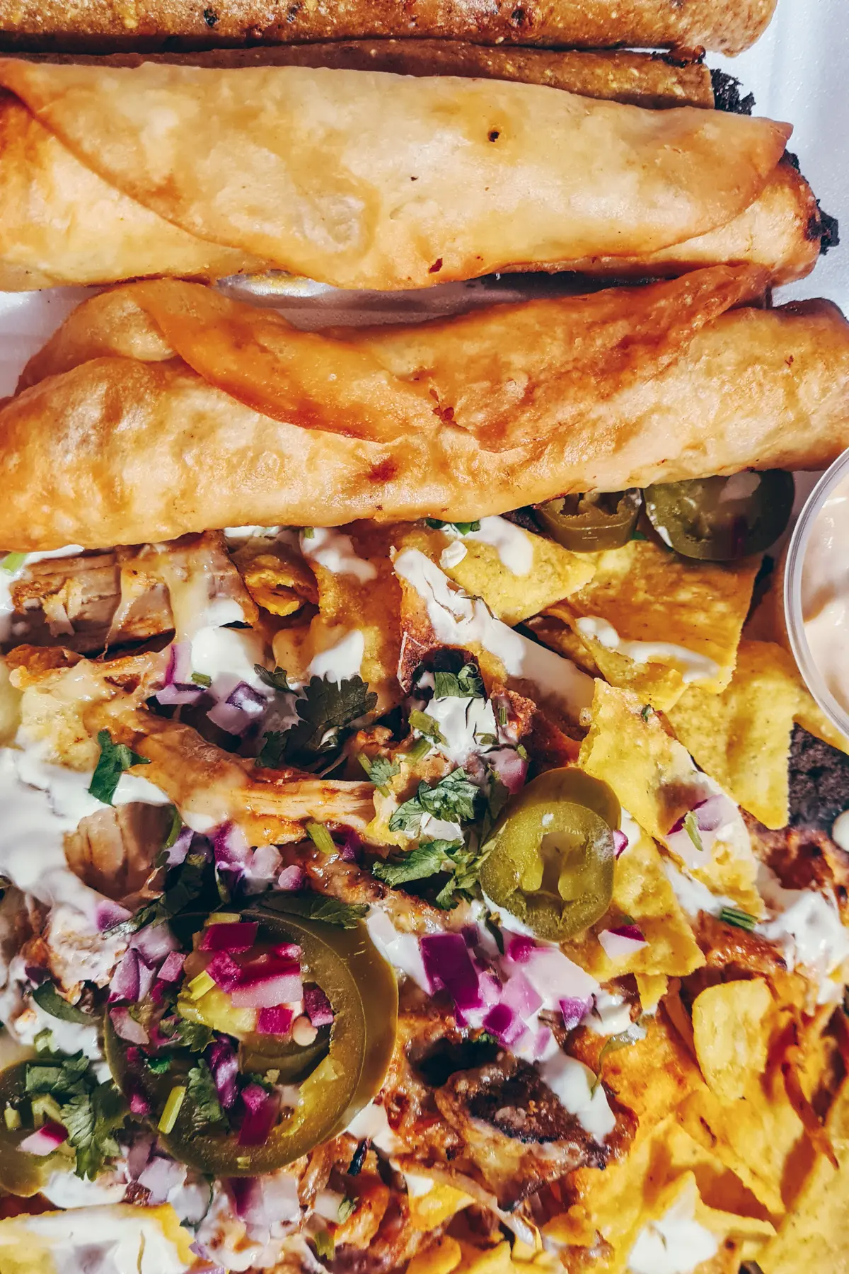 Close up of loaded nachos with pulled pork, red onion and Jalapeño next to golden taquitos at Manzana Mexican, one of the best restaurants in Krakow.