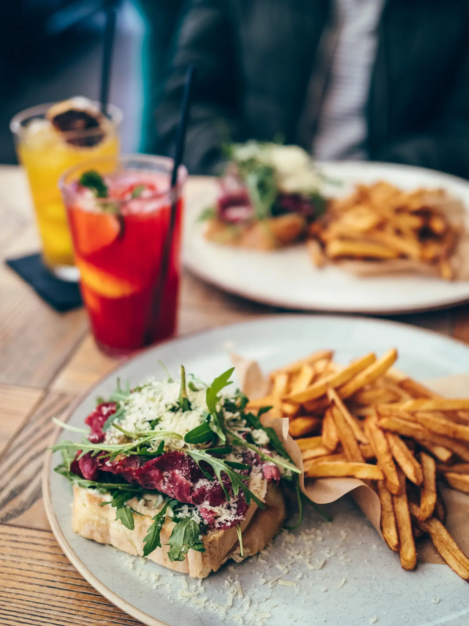 Toast with roast beef, arugula and parmesan on a grey plate with skinny fries, red and yellow lemonades in the background at Nova Resto Bar, one of the best restaurants in Krakow.