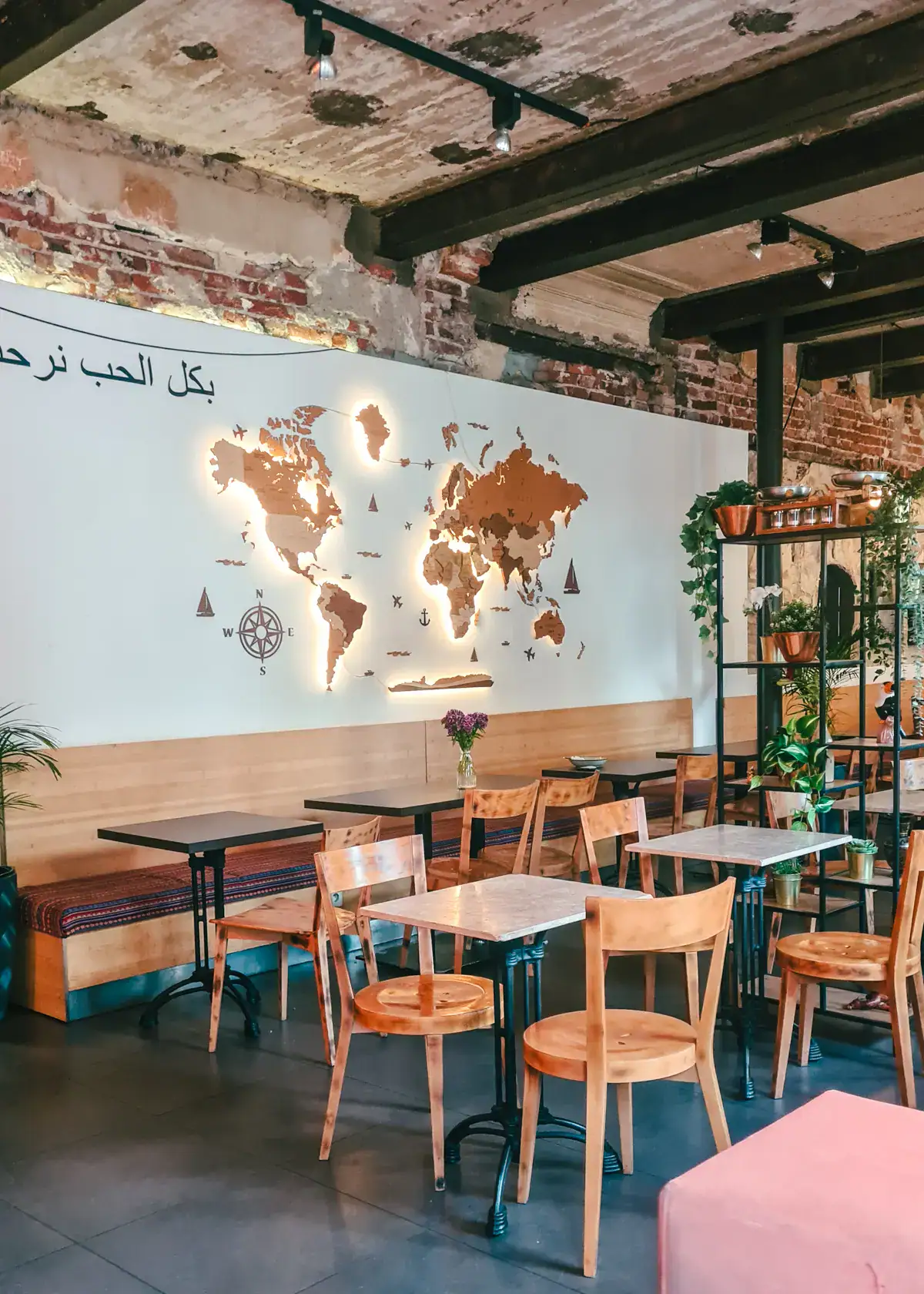 Wooden tables and chairs, and a bench along a white wall with a lit up wooden world map in the industrial looking Mazaya Vegan Restaurant in Krakow.