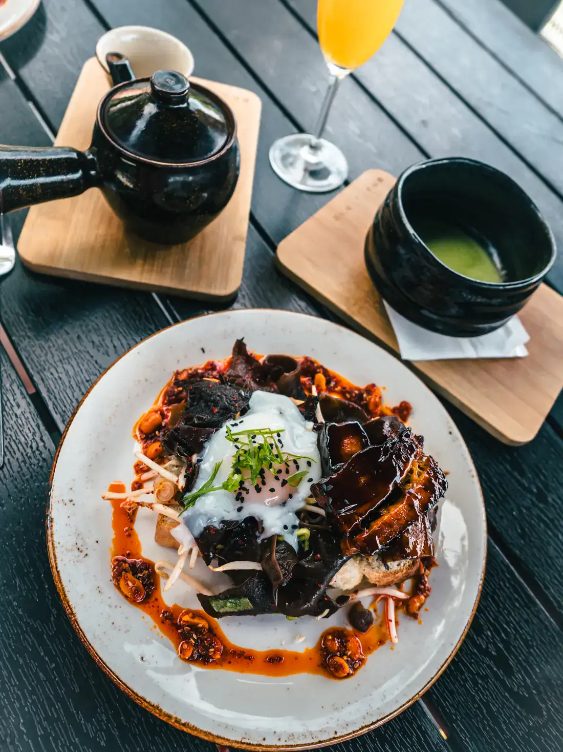 Japanese dish with and egg on toast with brown tare and a red bean sauce around, matcha and tea in the black bows in the background on a black table at Cafe Manggha, one of the most unique restaurants in Krakow.