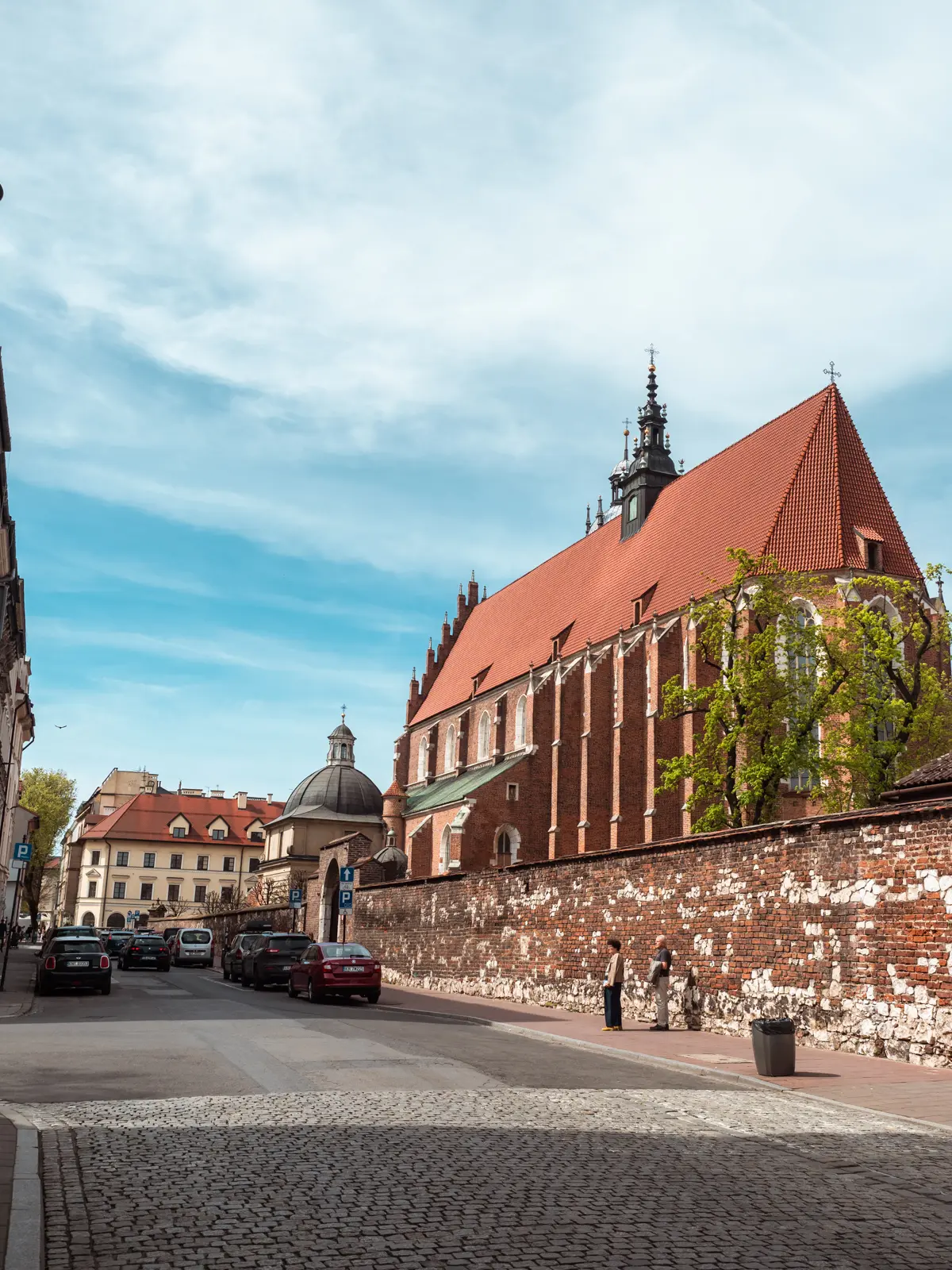 View of the majestic Corpus Christi Basilica in Kazimierz made from red brick and a cobbled street.