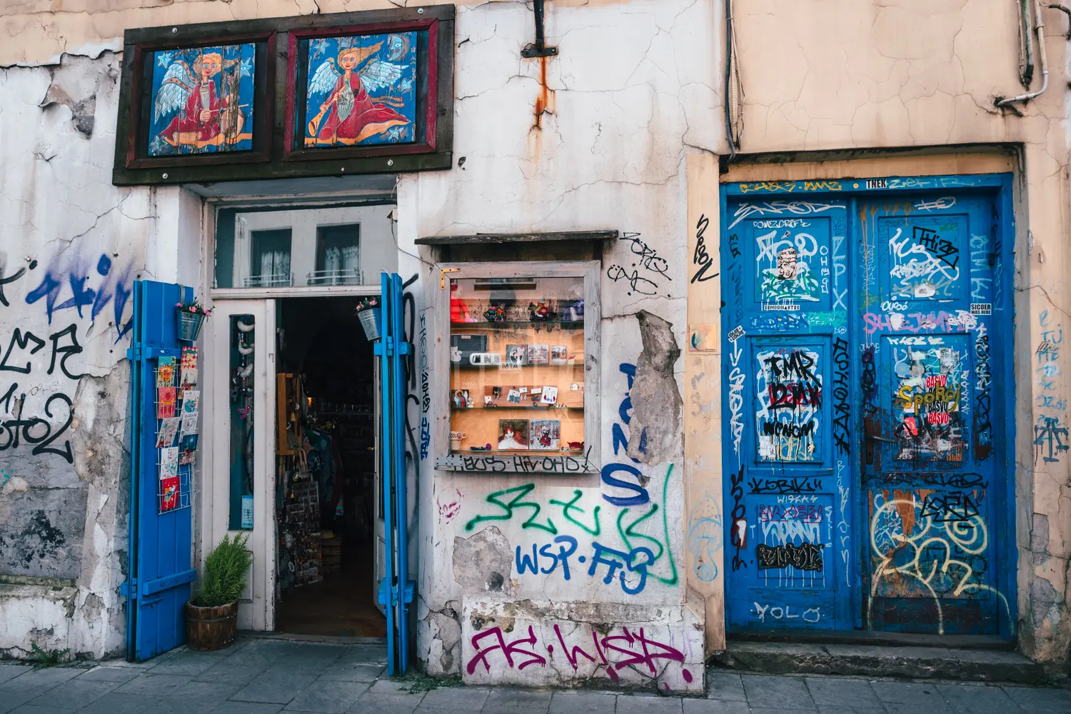 Entrance to a boutique in Kazimierz covered in graffiti, with a closed graffiti covered blue door on the right.