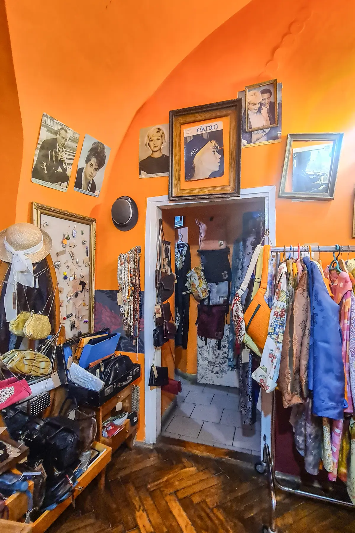 Inside on an orange vintage shop with pictures, purses and hats on the wall with racks of clothing, Inspiro Vintage shop in Kazimierz.