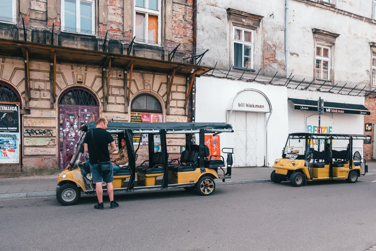 Two yellow and black tour buggies on a typical rough looking street in Kazimierz with graffiti on the wall. Best Kazimierz tours.