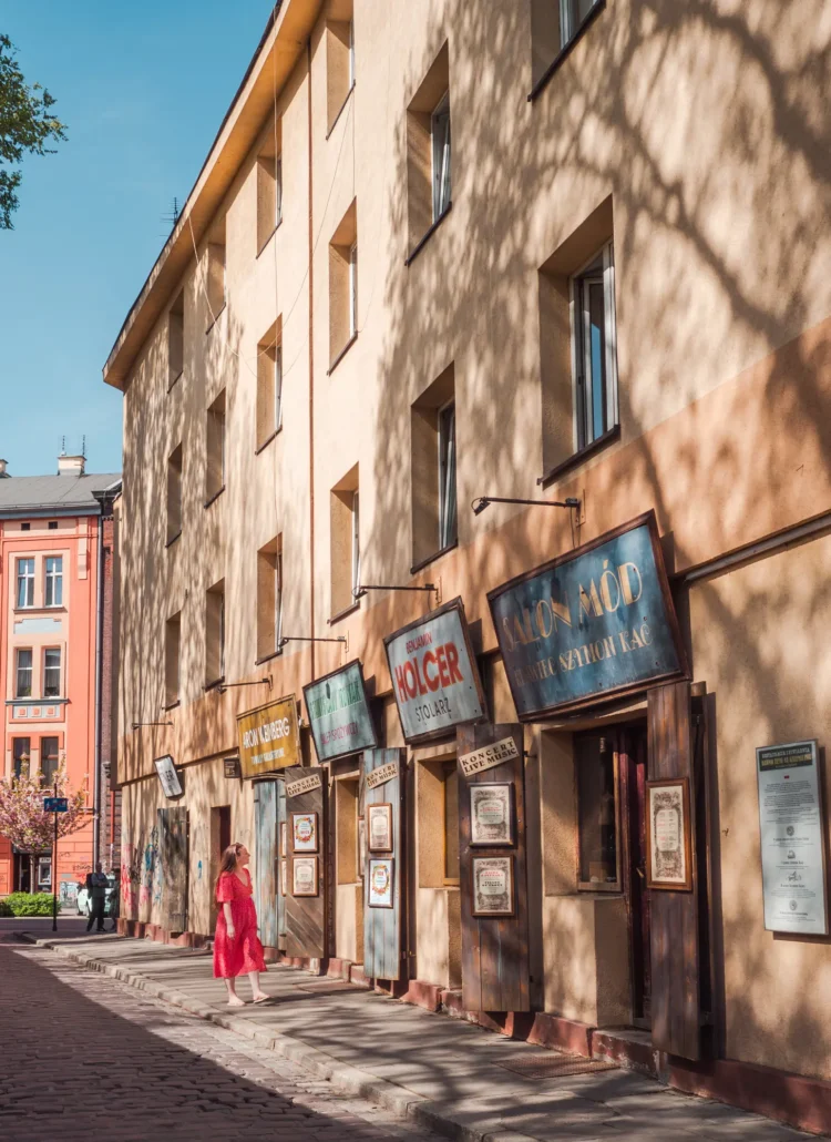 Woman in a red dress walking along a beige building with vintage Jewish restaurant signs in Kazimierz, Krakow.