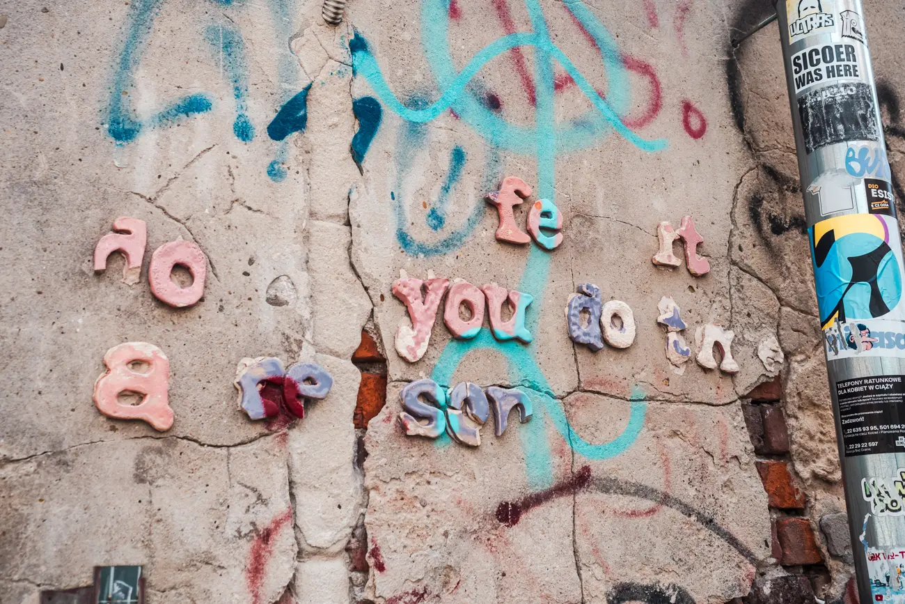 Close up of pink letters and turquoise graffiti on a crumbling wall in Kazimierz.