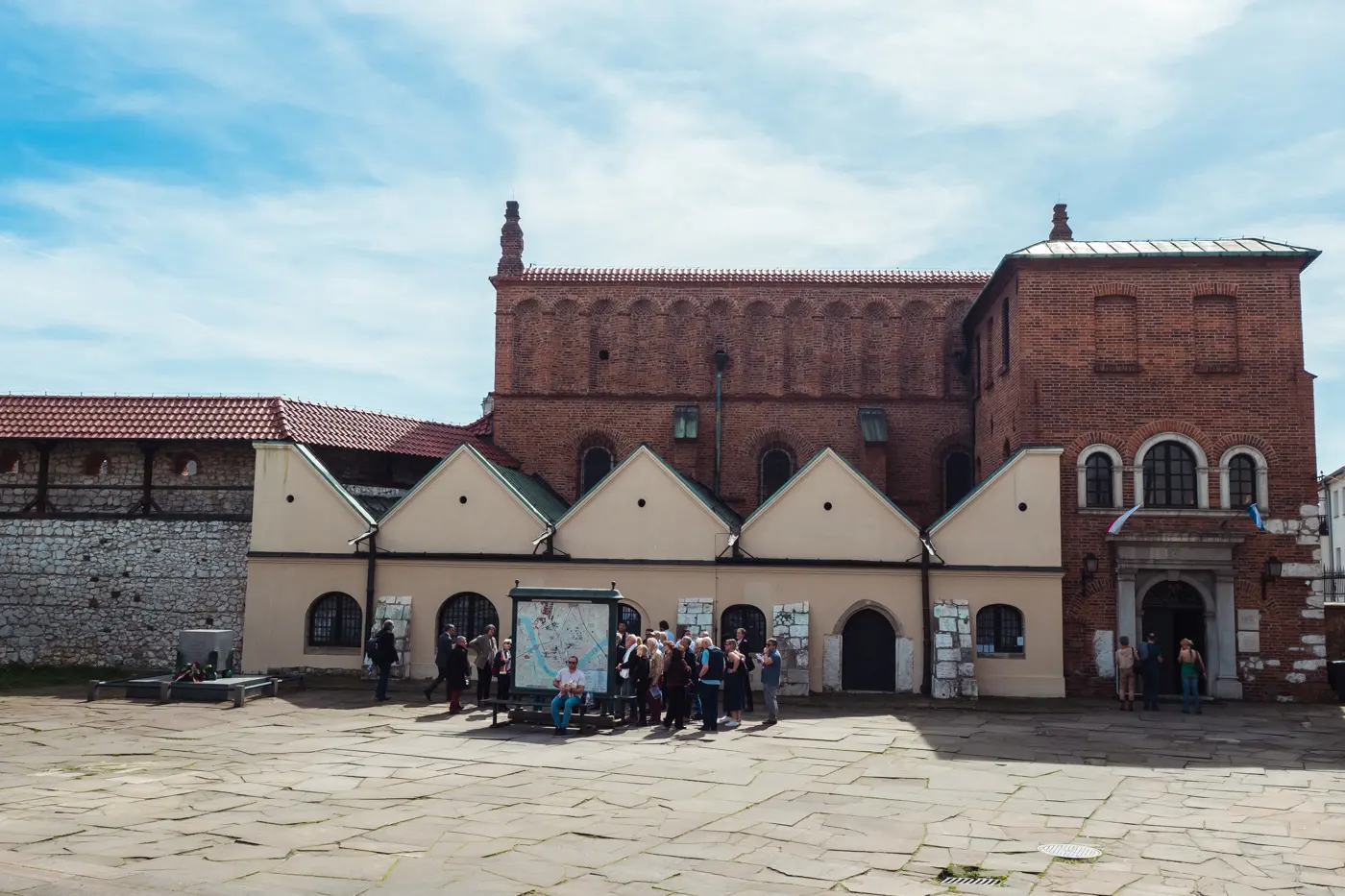 Group of people looking at a map outside the Old Synagogue made from red brick in Kazimierz Krakow on a sunny day.
