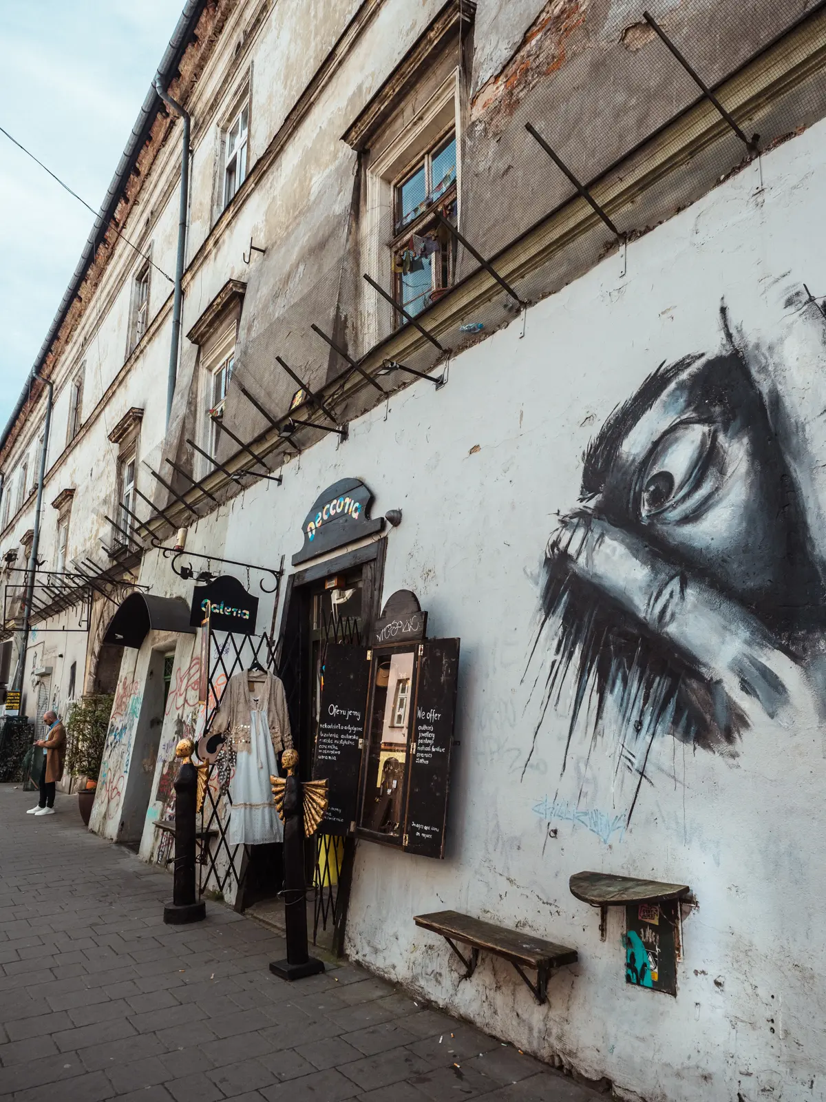 Entrance to a boutique in Kazimierz on a white wall with a black and white mural of an eye looking between two fingers.