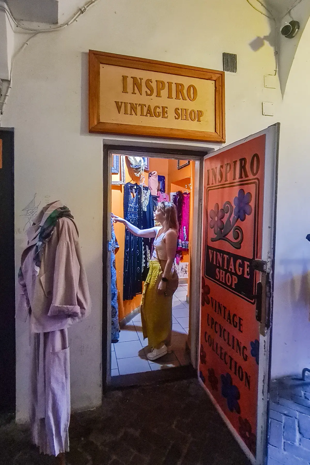 Woman wearing a white top and long yellow skirt standing in the entrance of Inspiro Vintage Shop in Kazimierz. 