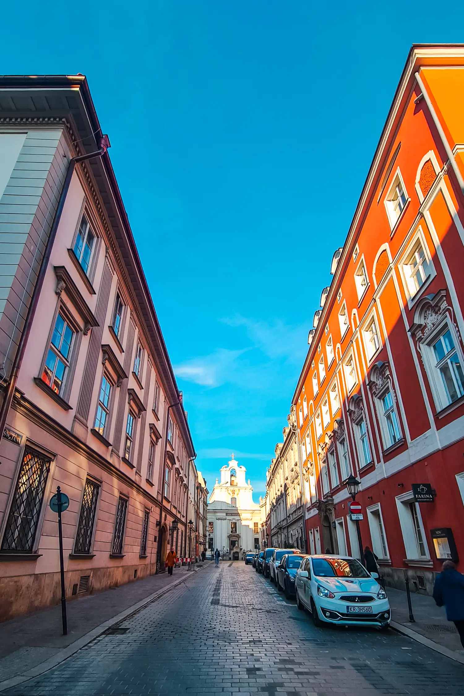 Typical street in Krakow, pink old building on the left, red old building on the right with a small white church in the middle, Krakow Airport to city center.