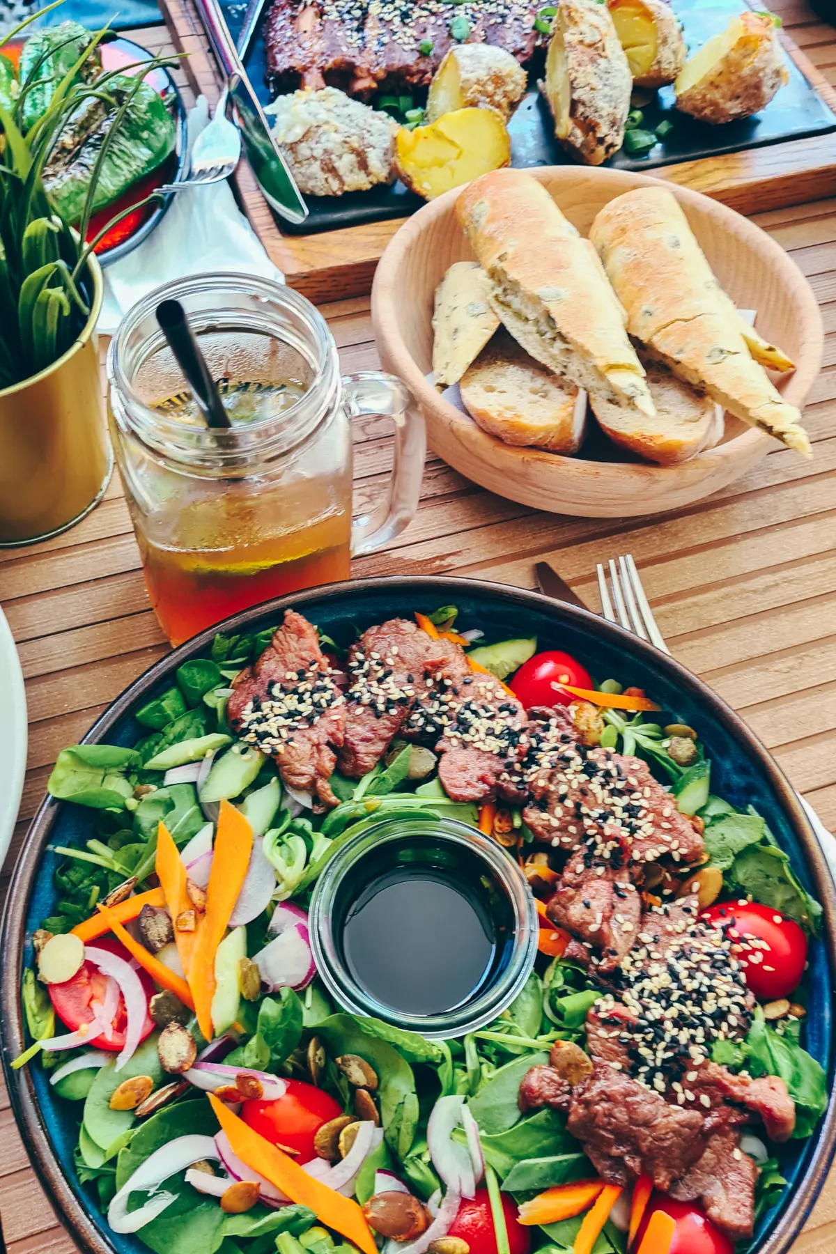 Beef salad in a large black bowl with teriyaki sauce in the middle, wooden bow of bread and a half full glass of iced tea, at Plac Nowy 1, one of the best restaurants in Krakow.