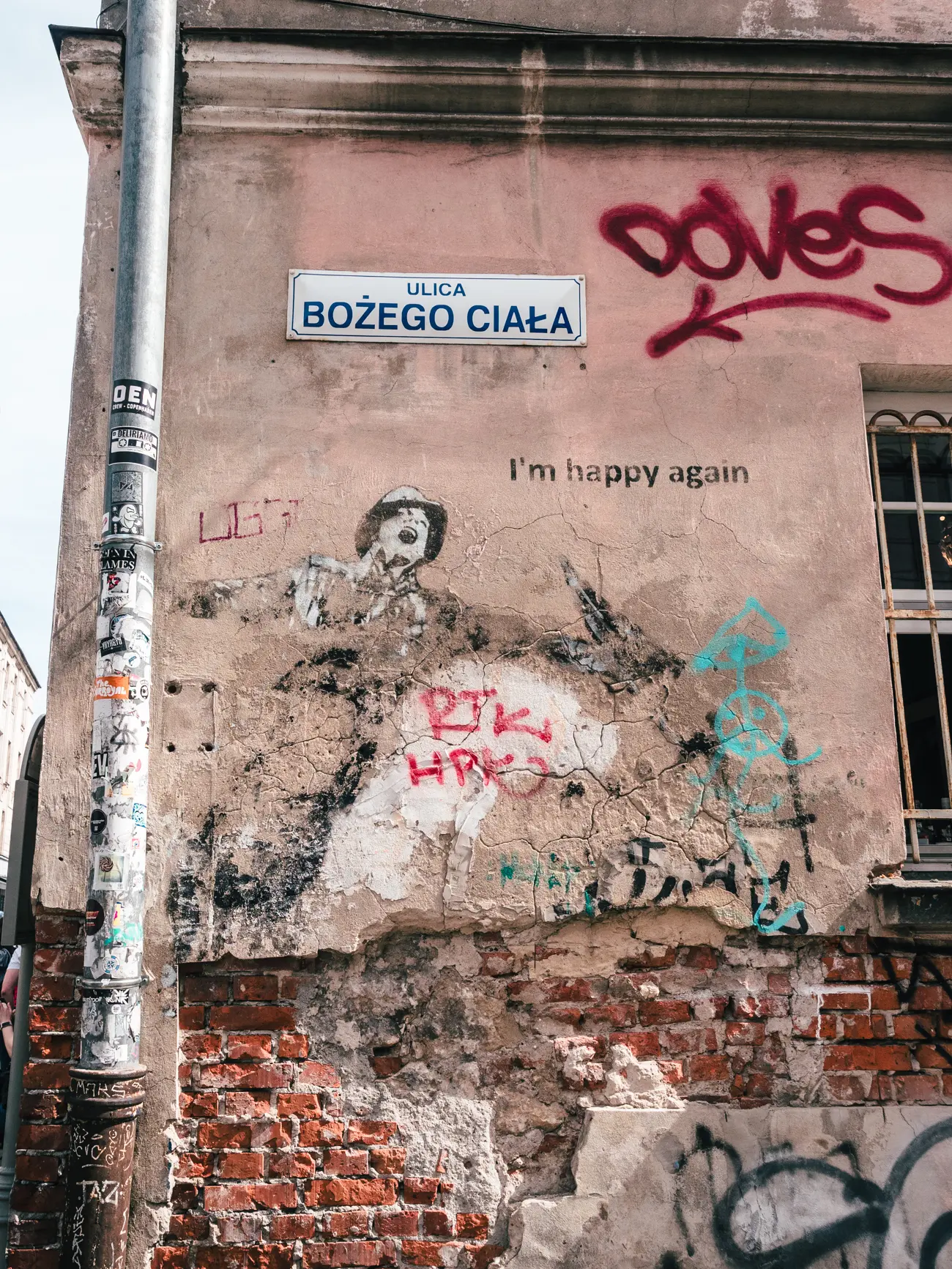 Faded graffiti and mural of a happy man singing while holding on to a street light on a crumbling wall in Kazimierz, Krakow.