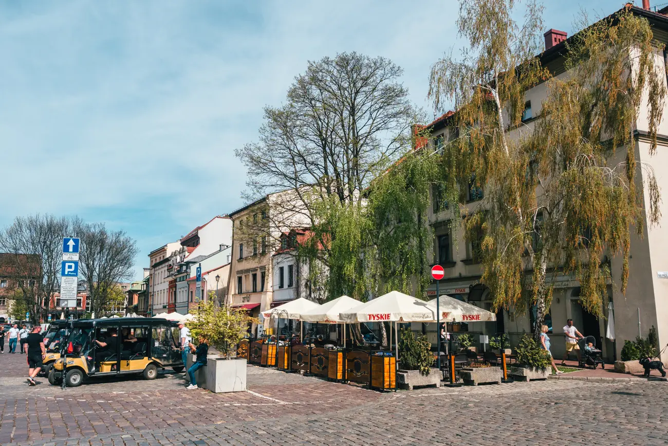 The cobbled Szeroka Street lined by Jewish restaurants covered in greenery and tour carts in the heart of Kazimierz.