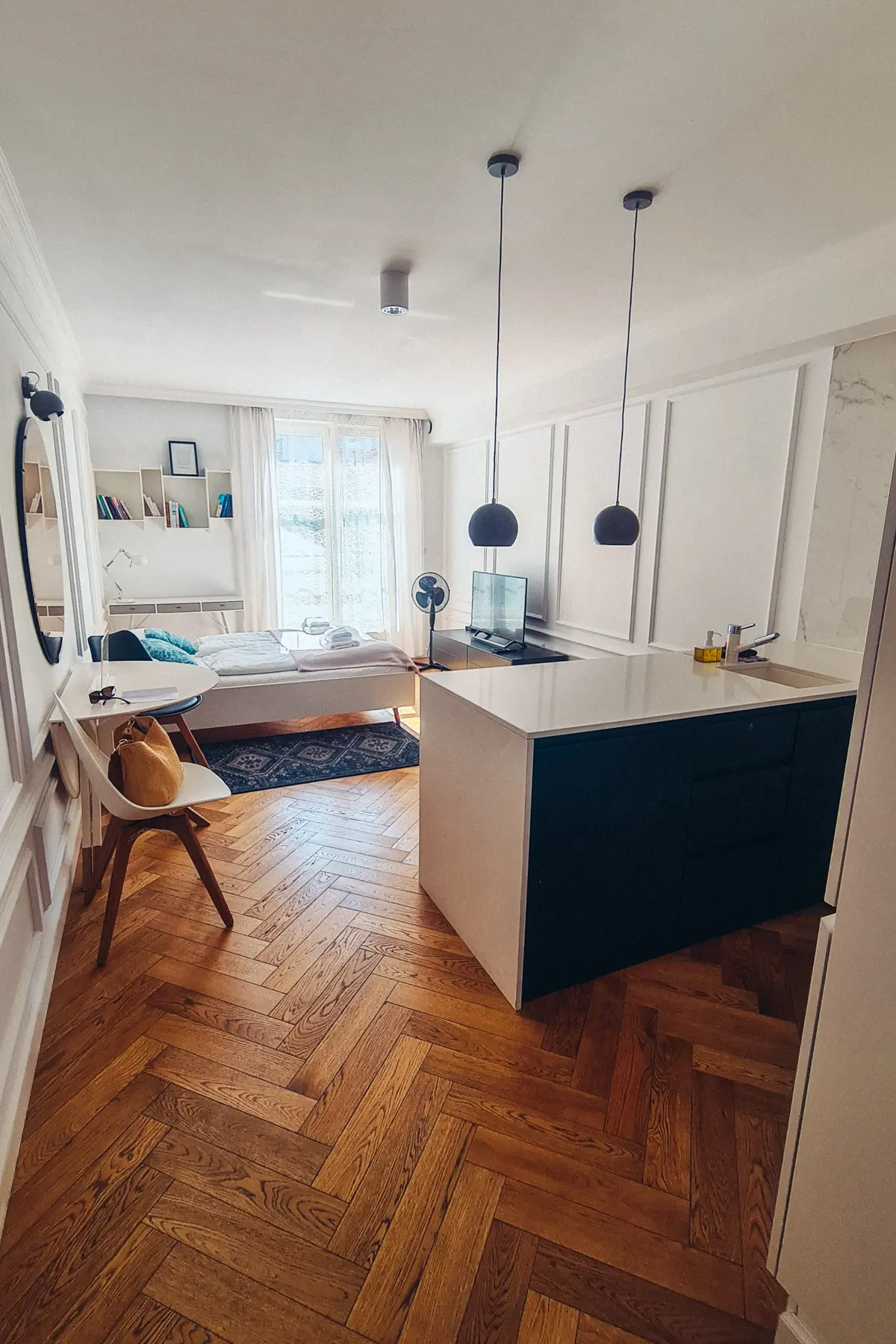 View from the entrance of a modern apartment in Kazimierz with herringbone floors, a black kitchen island and white paneled walls, one of the best places to stay in Krakow.