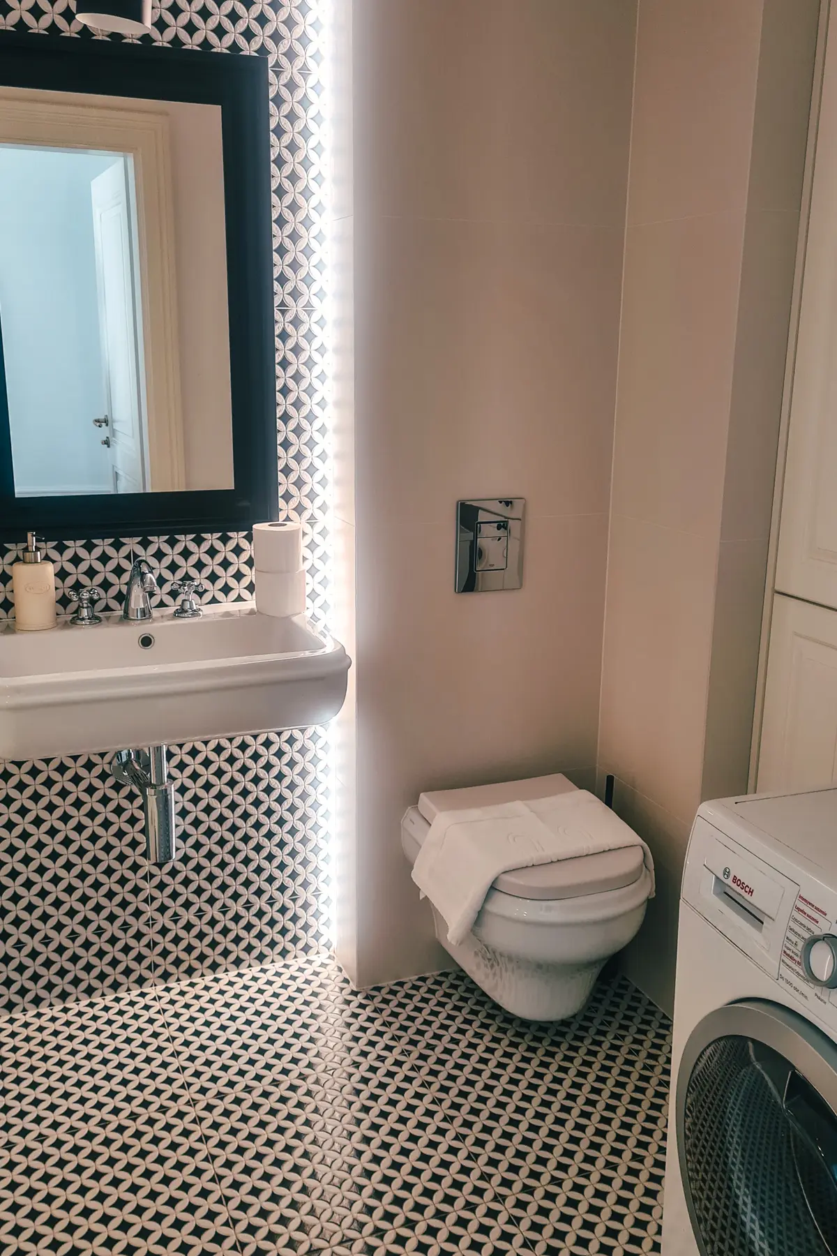 Bathroom with black and white tiled floors, black mirror, large ceramic sink and a washing machine, one of the best apartments to rent in Kazimierz Krakow.