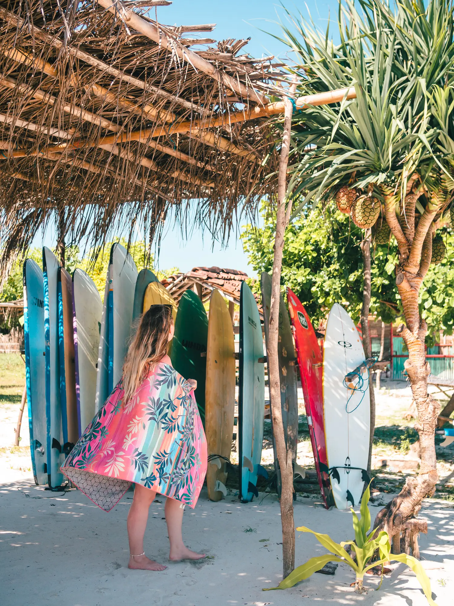 Woman with long hair standing in front of a rack of surfboards under a straw shack in Kuta, Lombok or Bali.