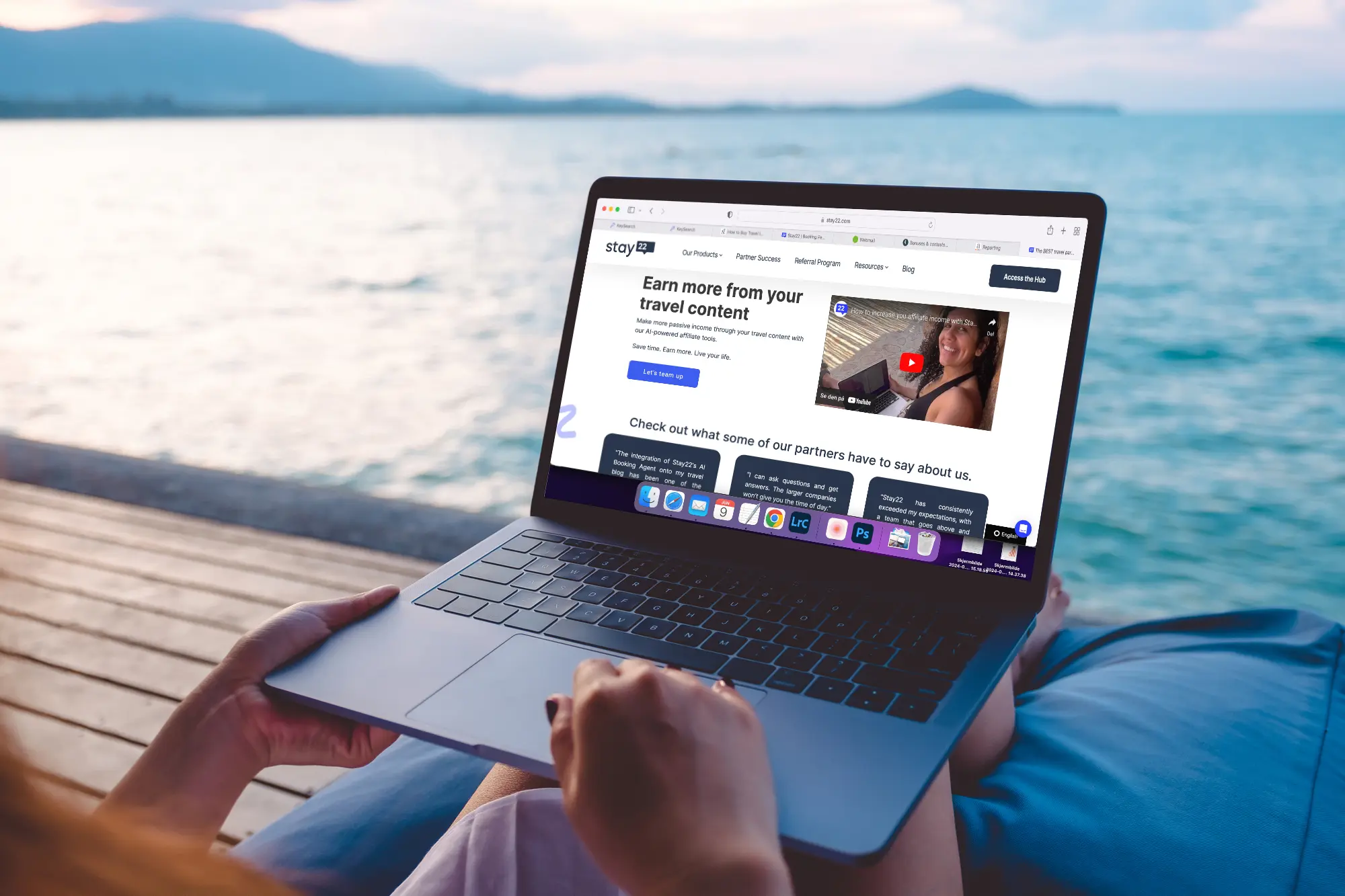 Close up of a computer with the Stay22 review open on the lap of a woman sitting on a blue bean bag on a pier at sunset.