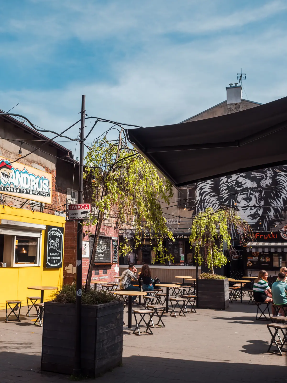 Judah Food Market with a yellow food truck, people sitting around tables and white and black graffiti in the background, during a weekend in Krakow.