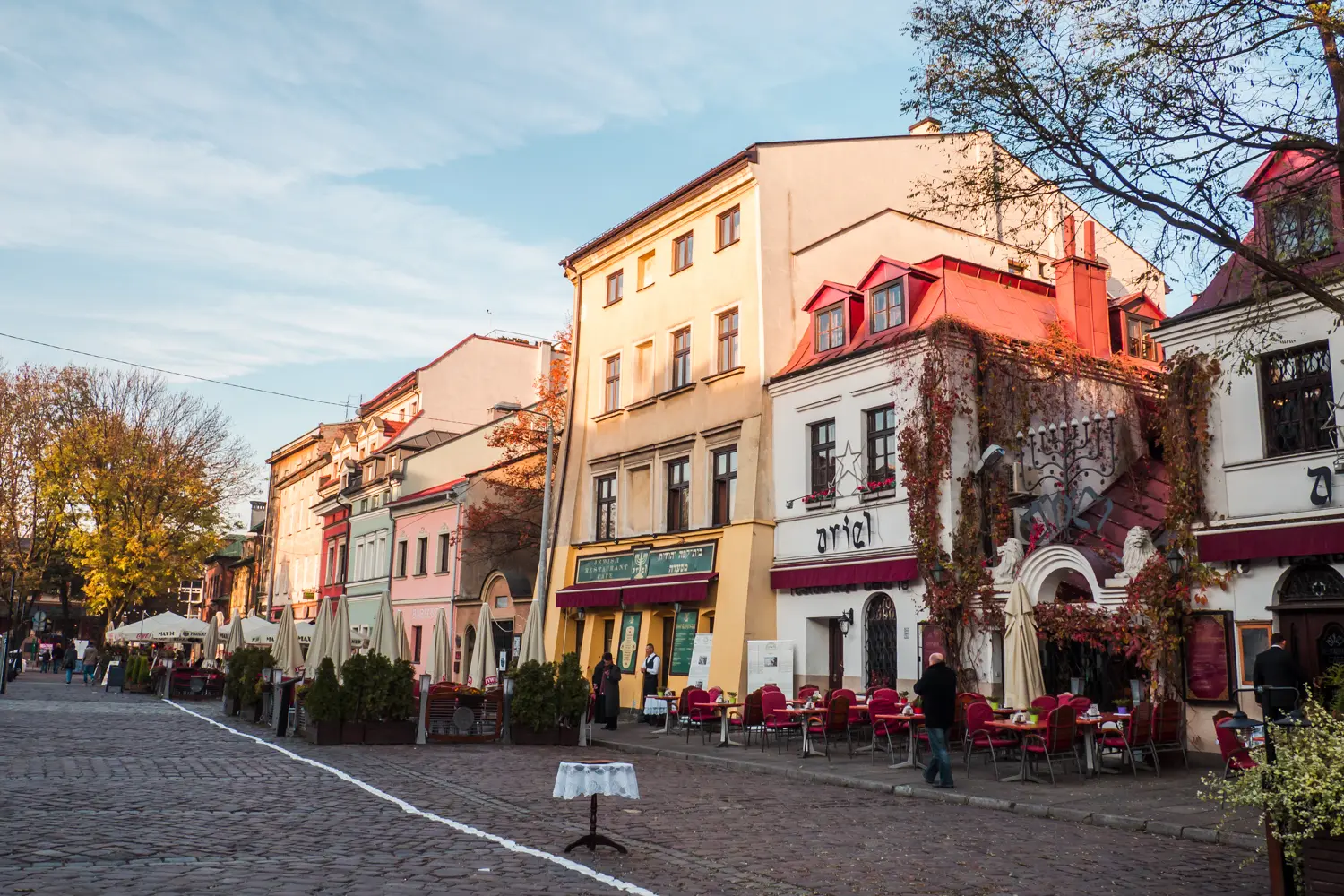 White, light yellow, pink and green Jewish restaurants next to each other on a cobbled square in the Jewish Quarter, Kazimierz, during a weekend in Krakow.