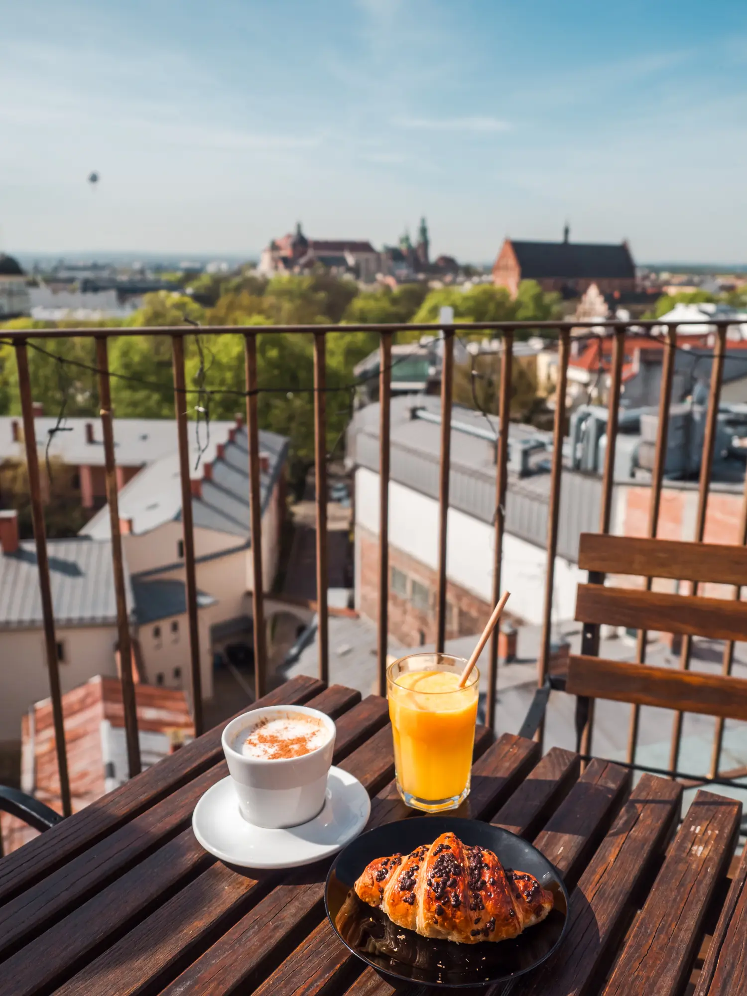 Coffee, orange juice and croissant on a wooden table at the Metrum Restobistro rooftop, a hidden gems during 2 days weekend in Krakow.