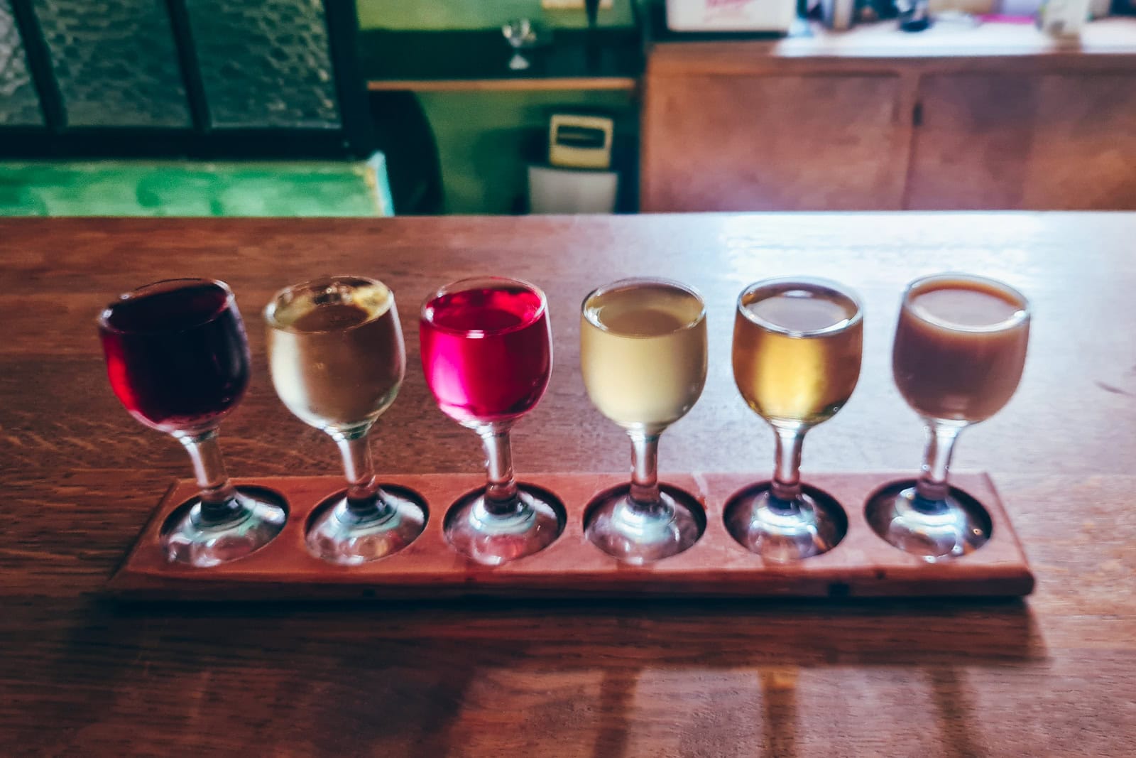 Six small shot glasses with different colored vodkas on a wooden plank, vodka tasting during a weekend in Krakow.