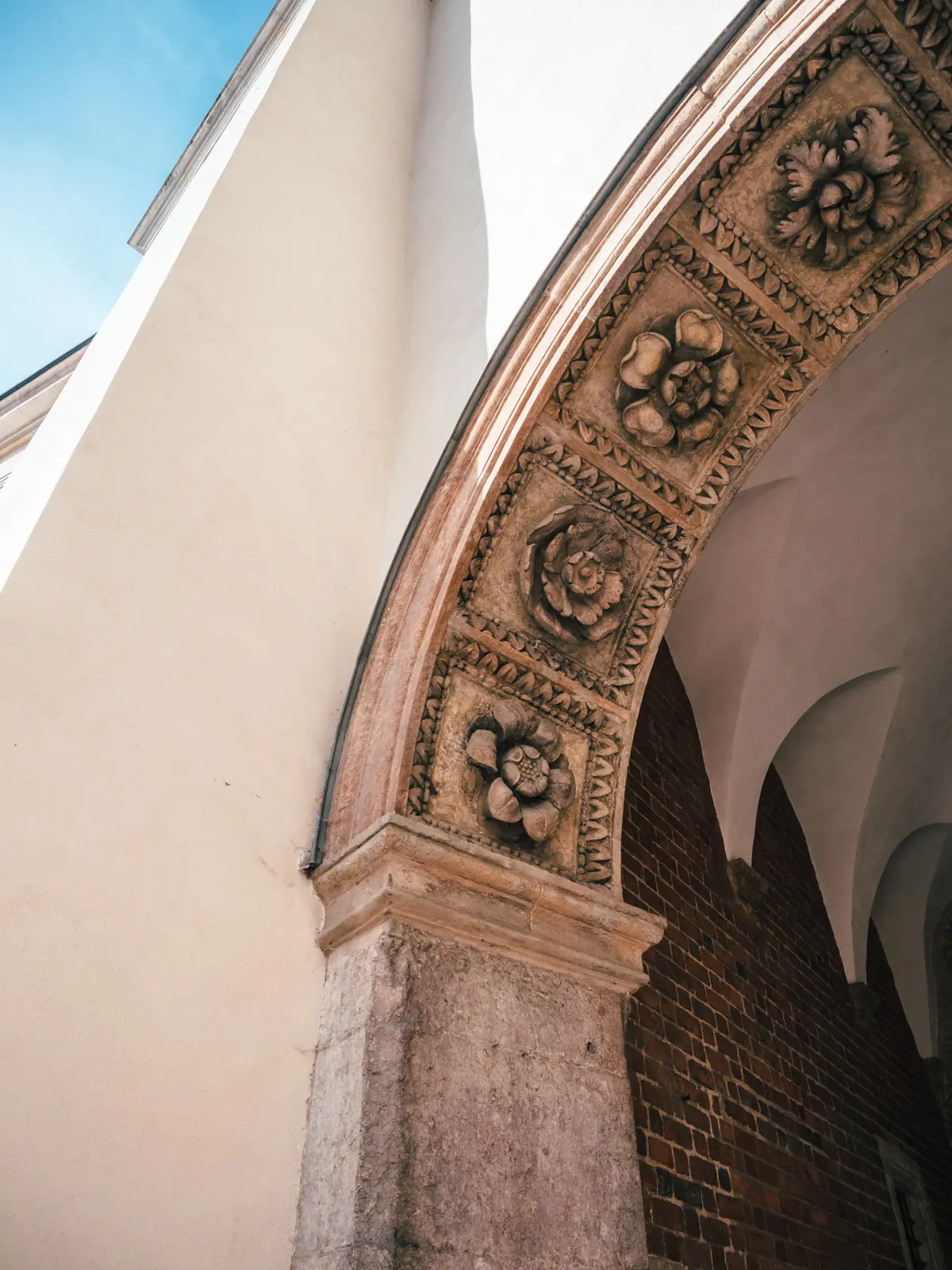 Sandstone colored archway with floral details and Wawel Castle in Krakow.