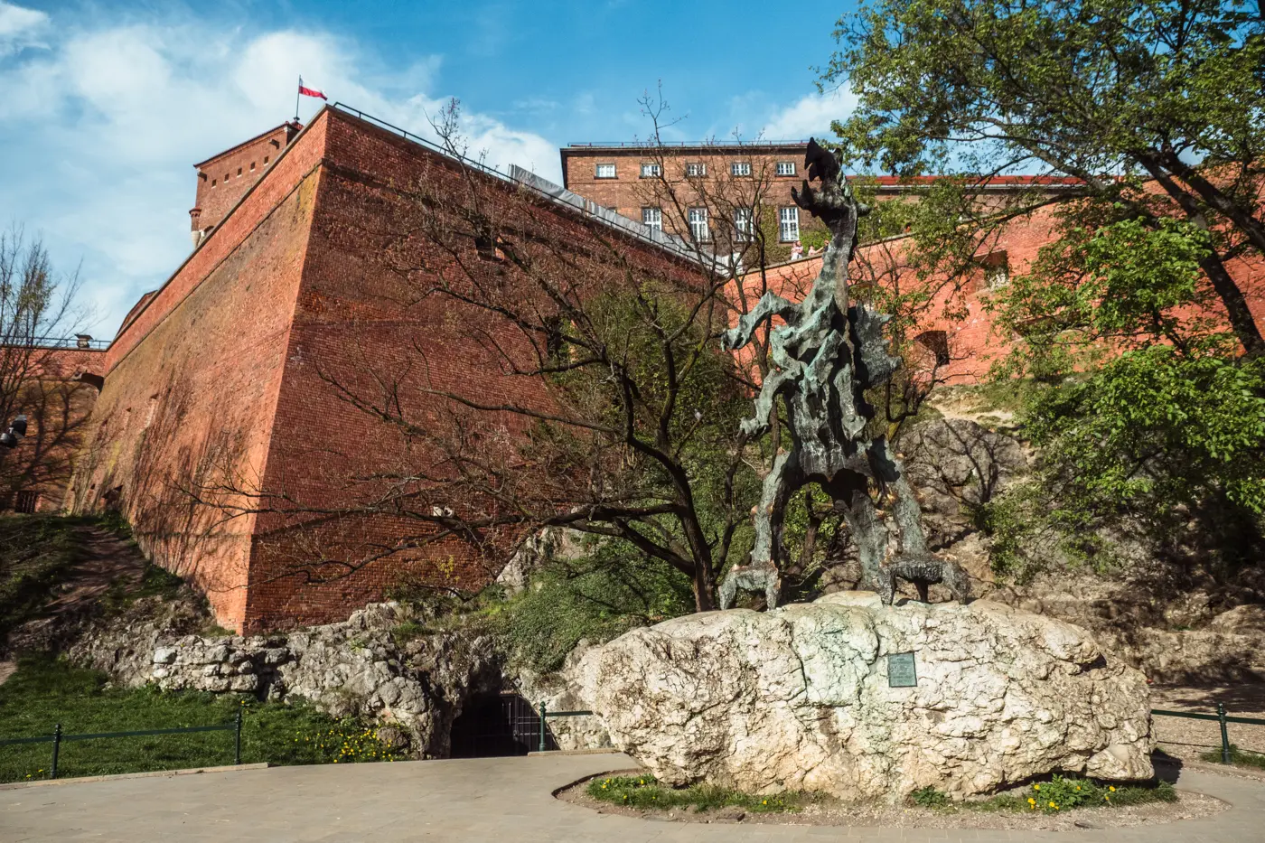 Metal dragon statue on a stone outside the red brick Wawel Castle Dragon's Den in Krakow.