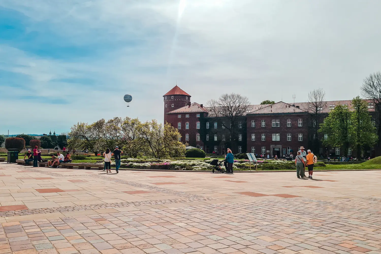 People walking around Wawel Castle grounds with the Visitors Center brick building and the Krakow Balloon in the background.