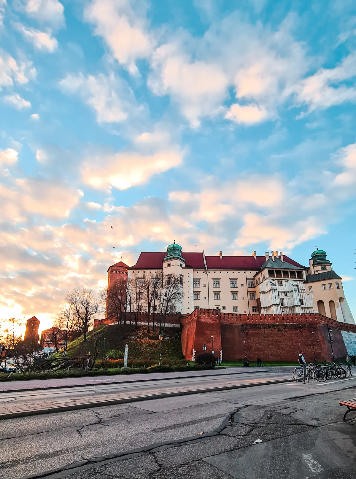 View of Wawel Castle on Wawel Hill from the street during sunset with pastel colored clouds on a blue sky.