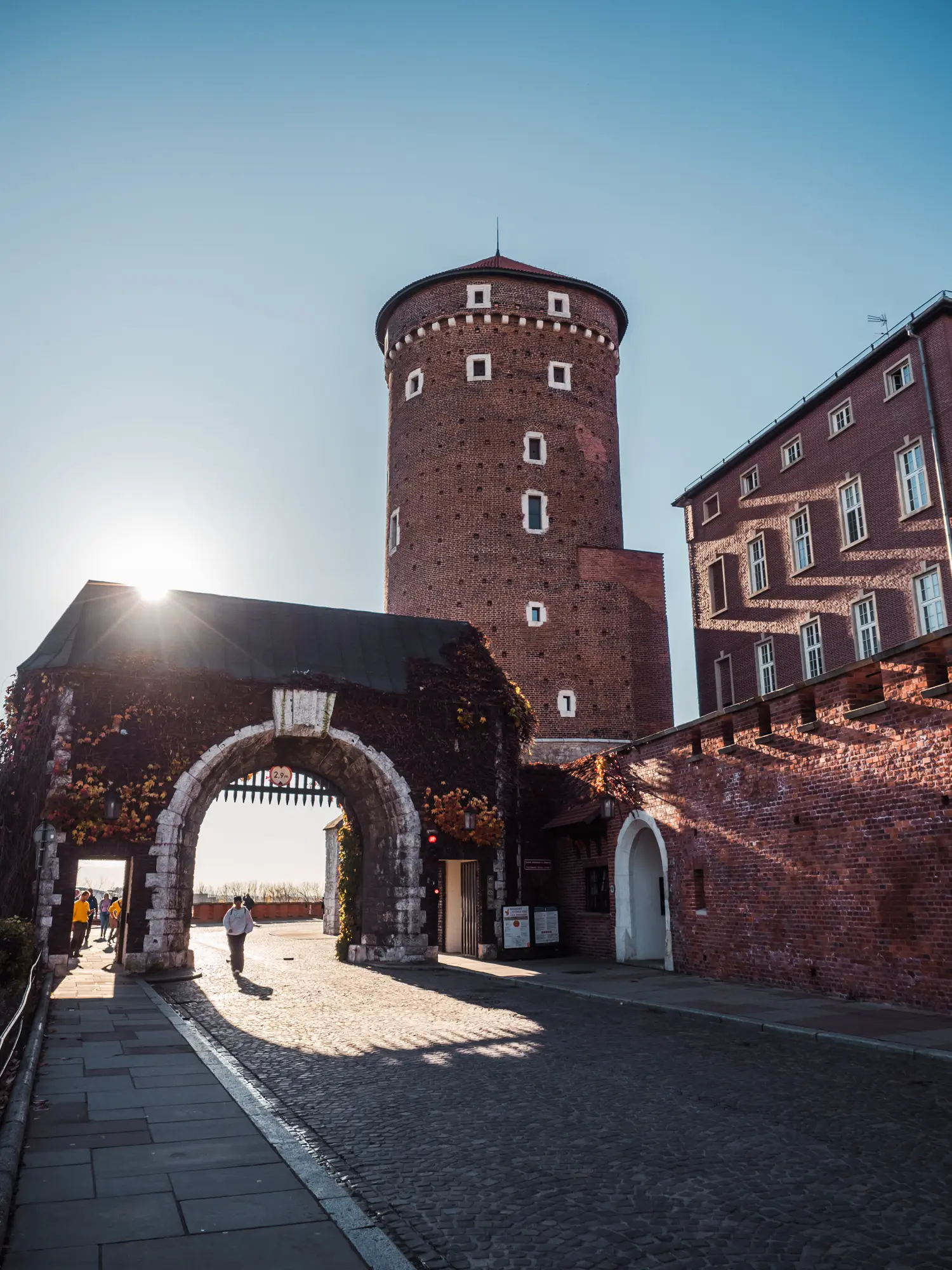 Sun shining into the arched gateway with a tower in the background at Wawel Castle in Krakow.