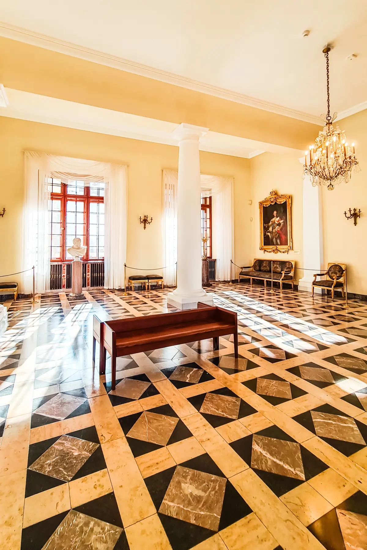 Yellow room with white pillars and a square patterned stone floor in the Royal Apartments at Wawel Castle.