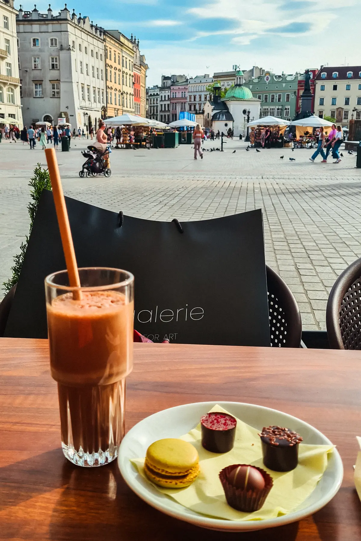 Cholocate drinks with a paper straw and four chocolate pieces on a green napkin on a table in Rynek Market Square during a weekend in Krakow.