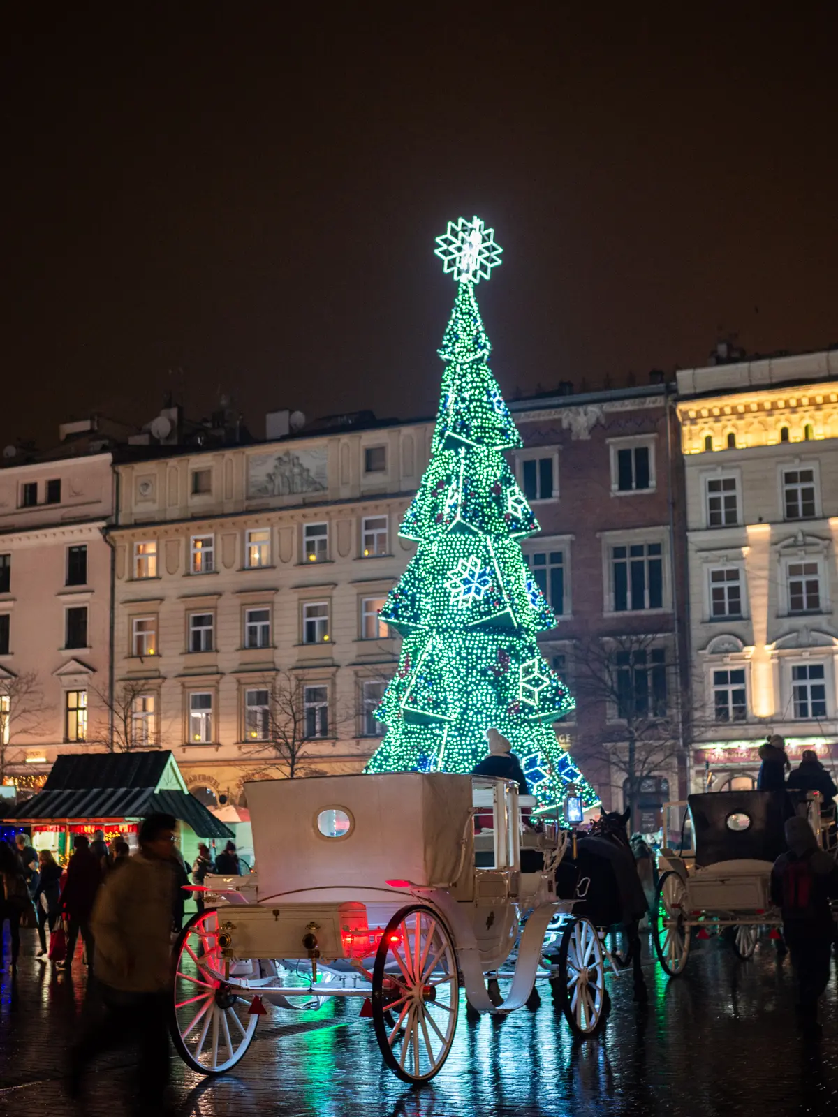 Horse and a white carriage in front of a Christmas tree covered in lights at the market square in Krakow Christmas Market.