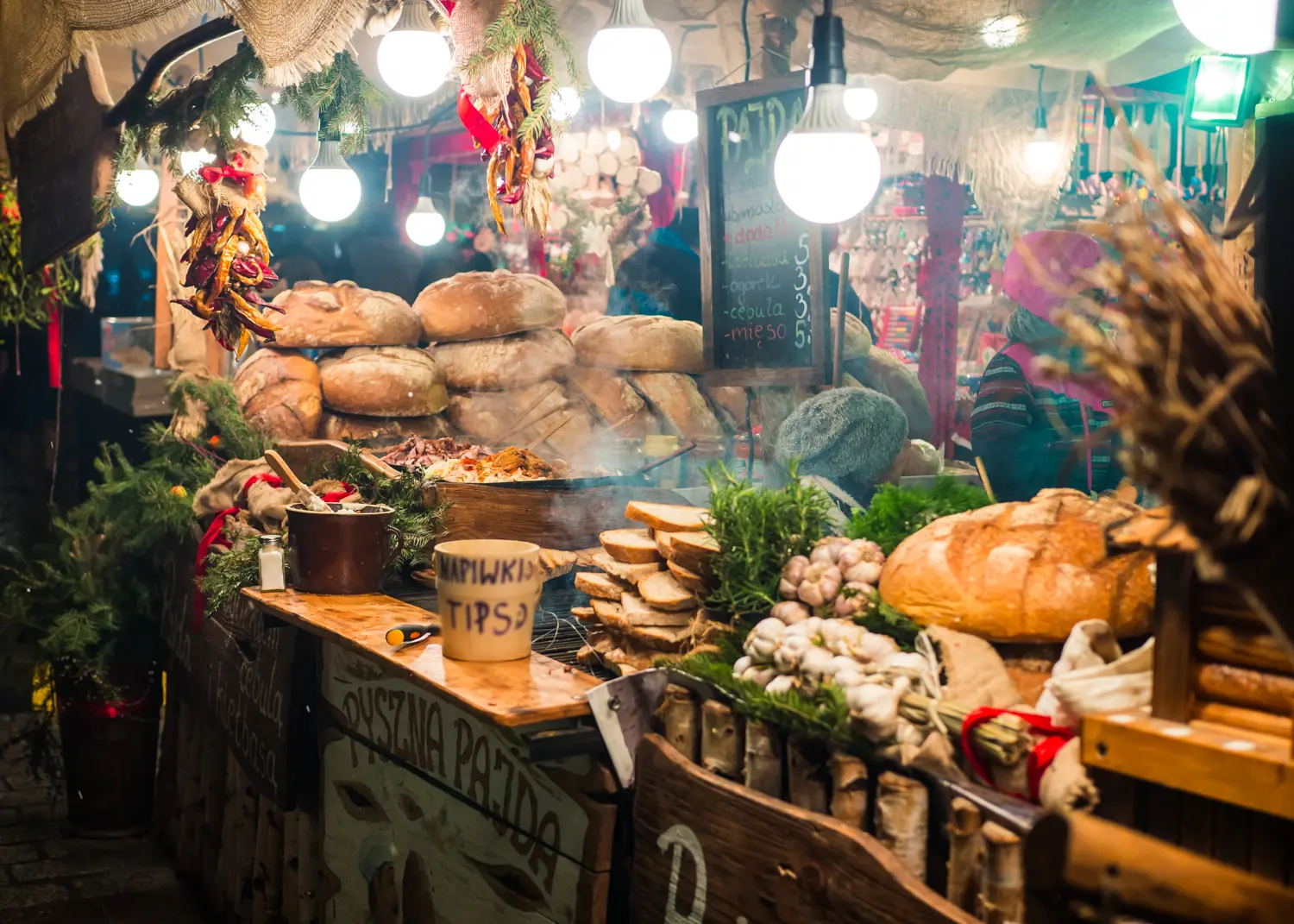 Close up of a food stall at Krakow Christmas Market, selling meat and bread, decorated with lights, red bows and spruce branches.