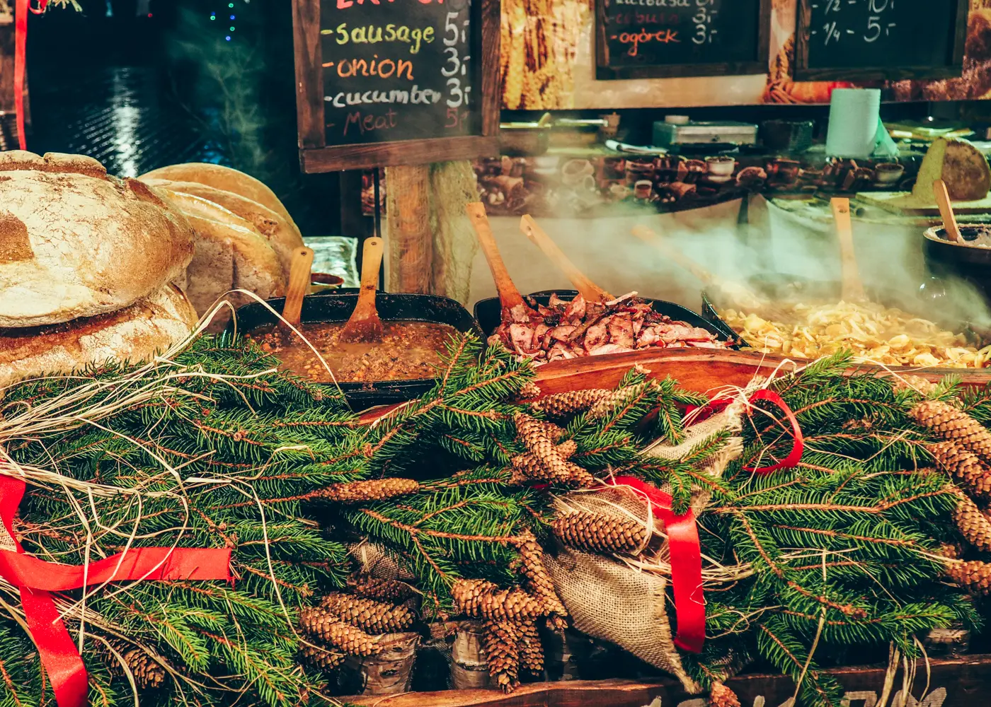 Close up of a food stall at Krakow Christmas Market, selling meat and bread, decorated with lights, red bows, spruce cones and branches.