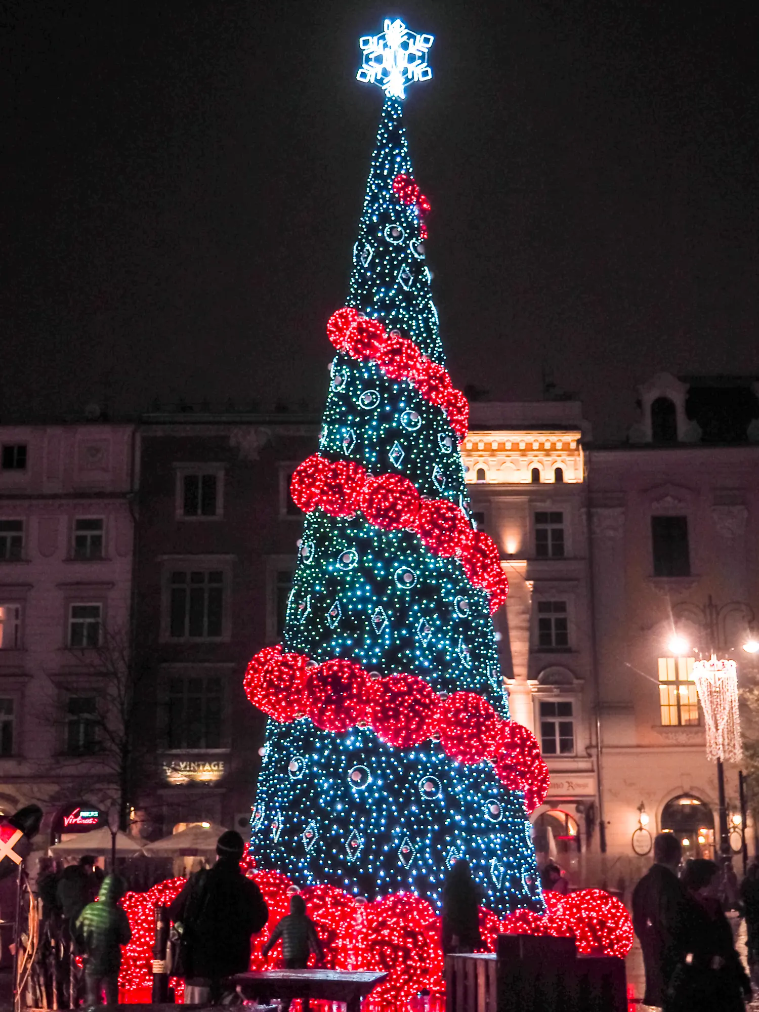 Cone shaped Christmas tree decorated with thick red garland and a snow flake star at Krakow Christmas Market at night.