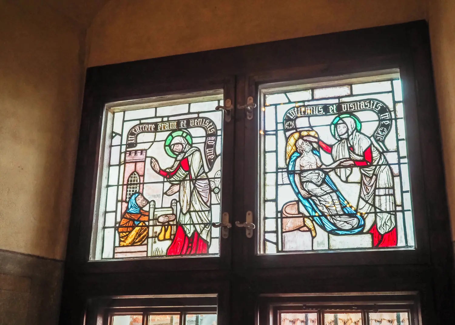 Two square stained glass windows depicting people in Malbork Castle.