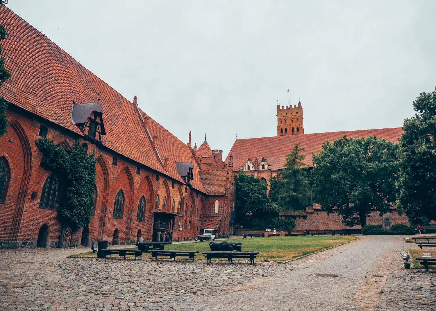 Cobbled courtyard with green trees in the middle of the massive red brick courtyard of Malbork Castle in Poland.
