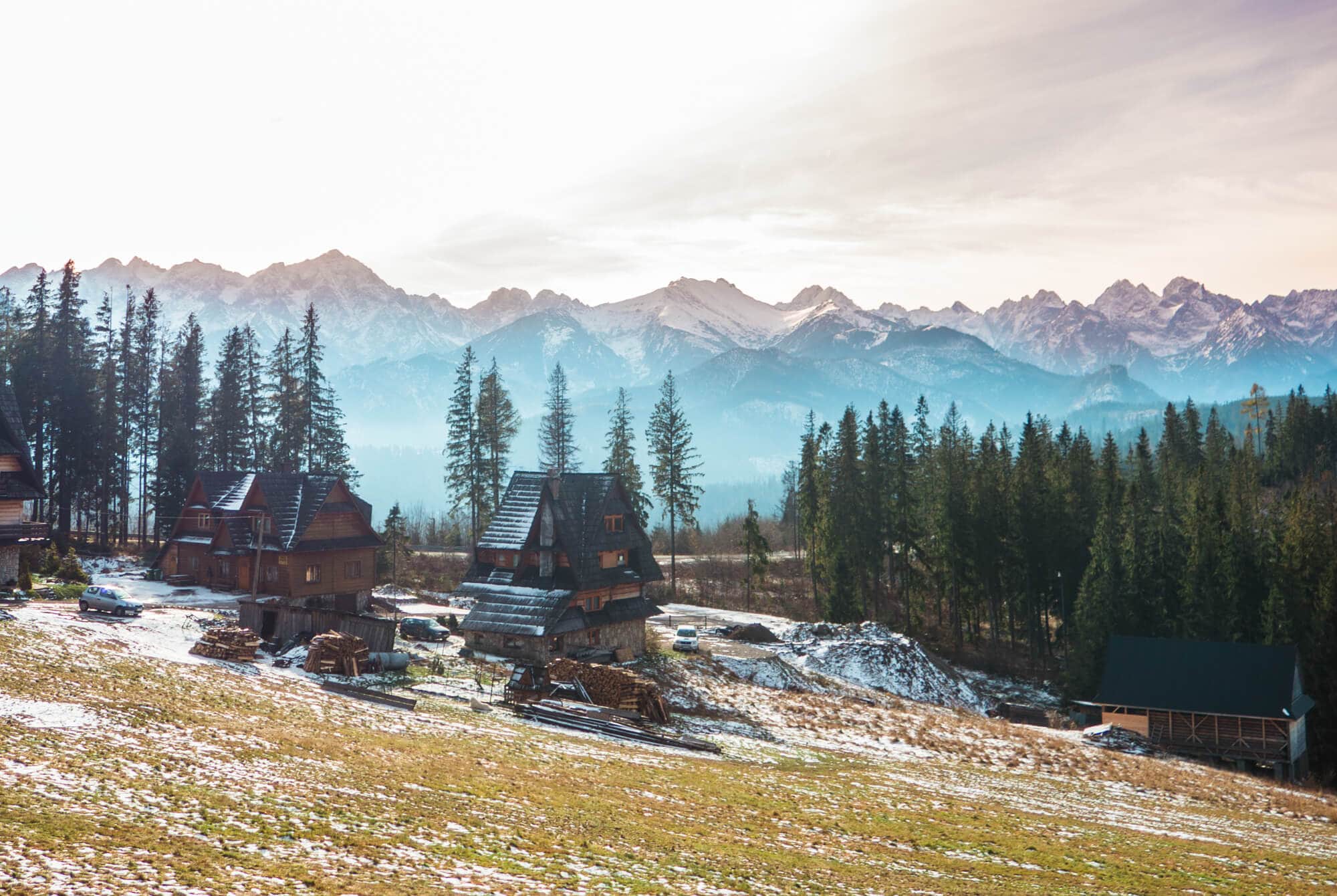 Two traditional Polish dark wood houses with steep black roofs on a field surrounded by trees with mountains in the background, on our way to Morskie Oko.